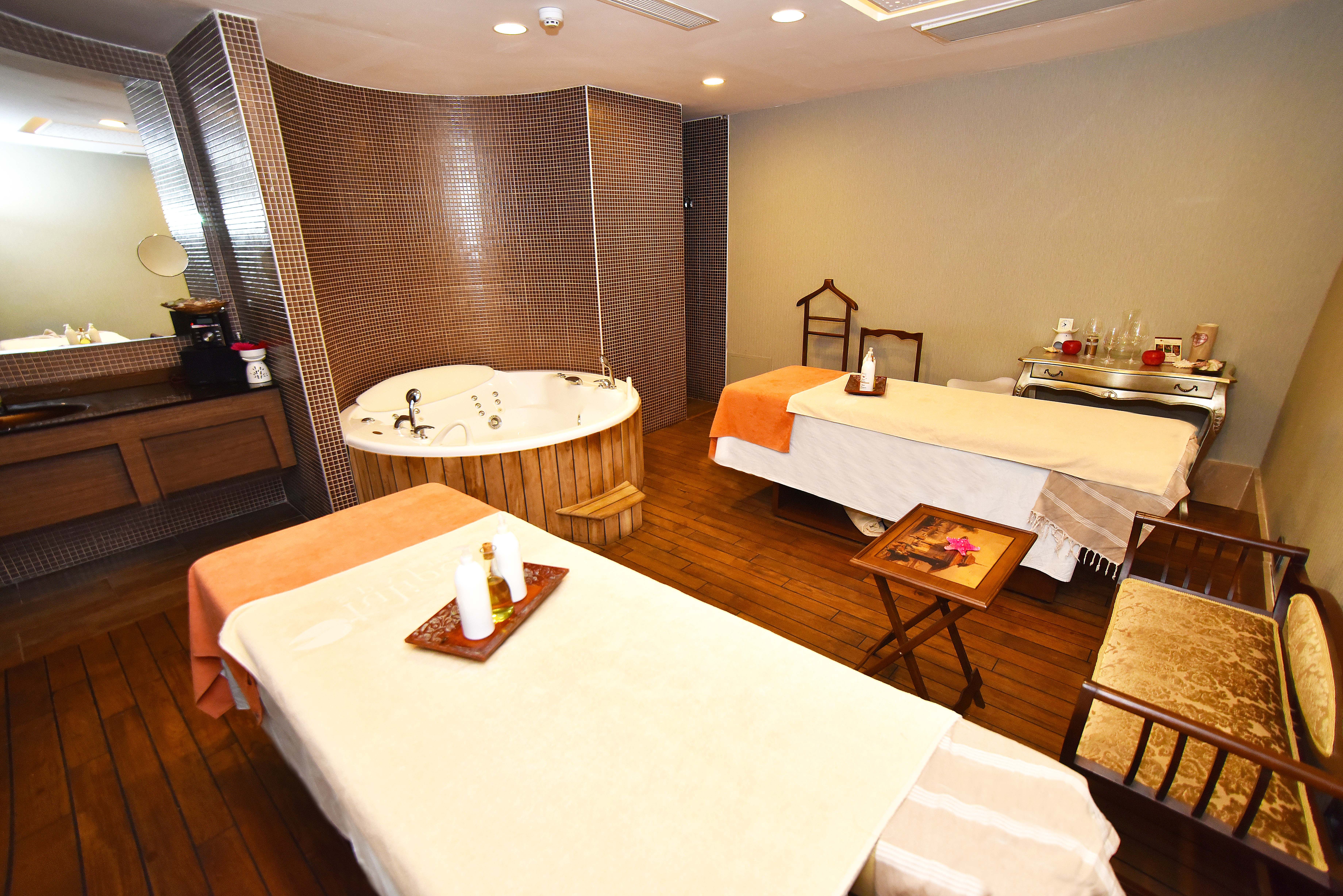 Two massage tables with orange towels and a jacuzzi with bamboo accents in a spa room.