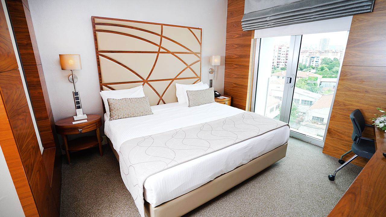 A king-sized bed with beige pillows and a patterned headboard in a hotel room.