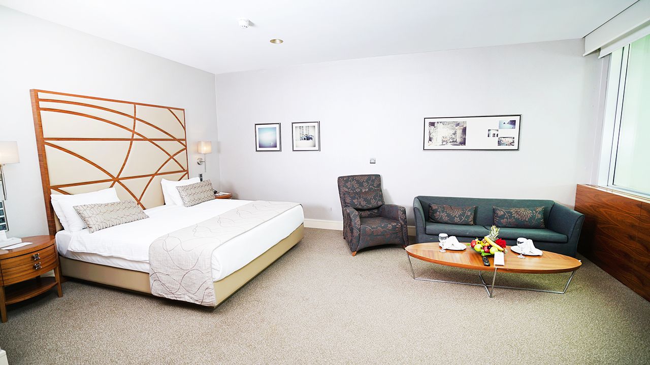 Spacious hotel suite with a king-size bed, armchair, sofa, and coffee table.