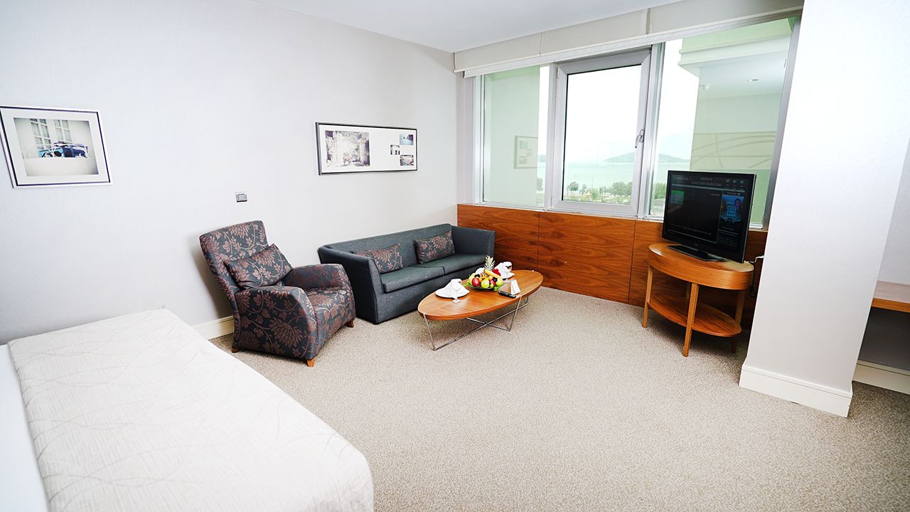 A hotel room with a bed, armchair, sofa, coffee table, and television.