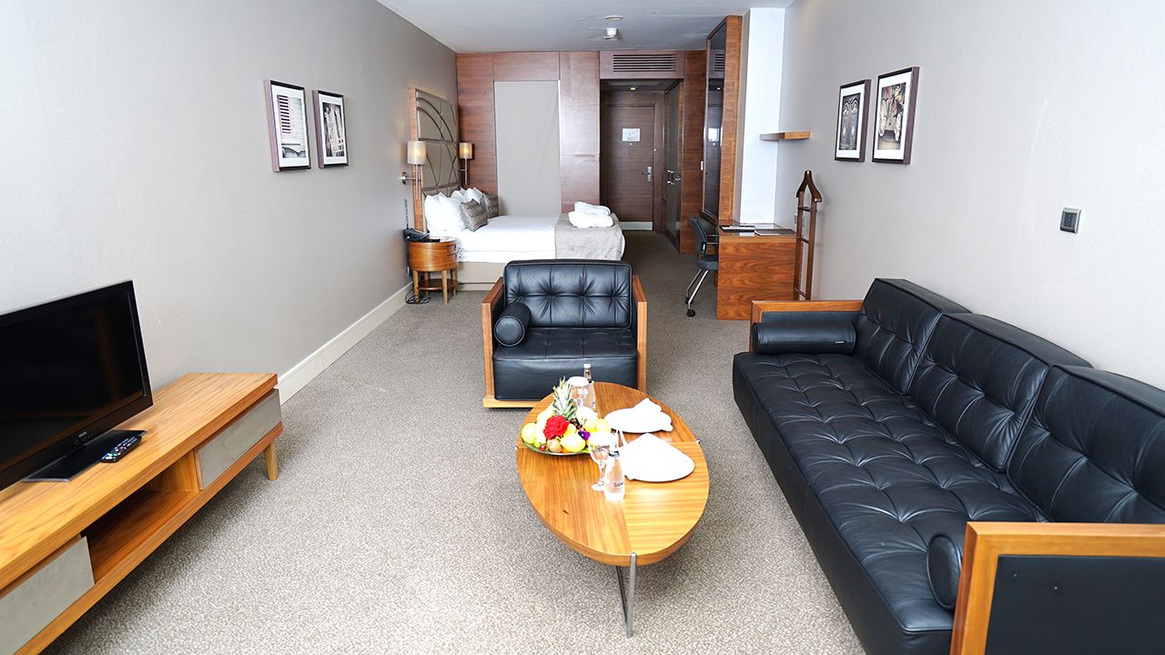 Contemporary hotel suite with a black leather couch, wooden furniture, and a comfortable bed.