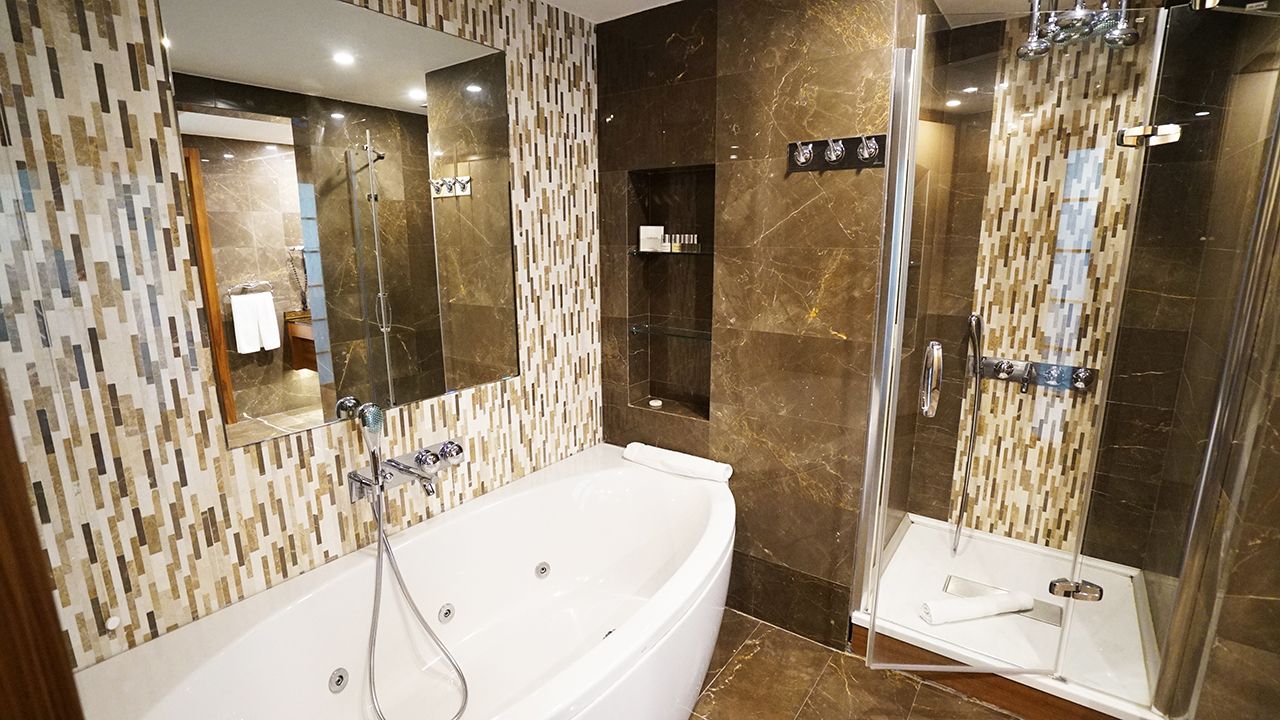 Modern bathroom featuring a white corner jetted tub, a separate glass shower, and elegant tiled walls.