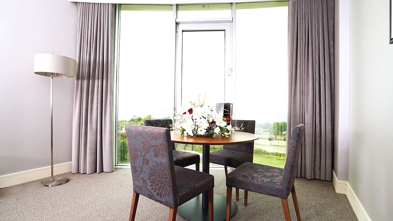 Modern room with round table, four chairs, floral centerpiece, and large window view.