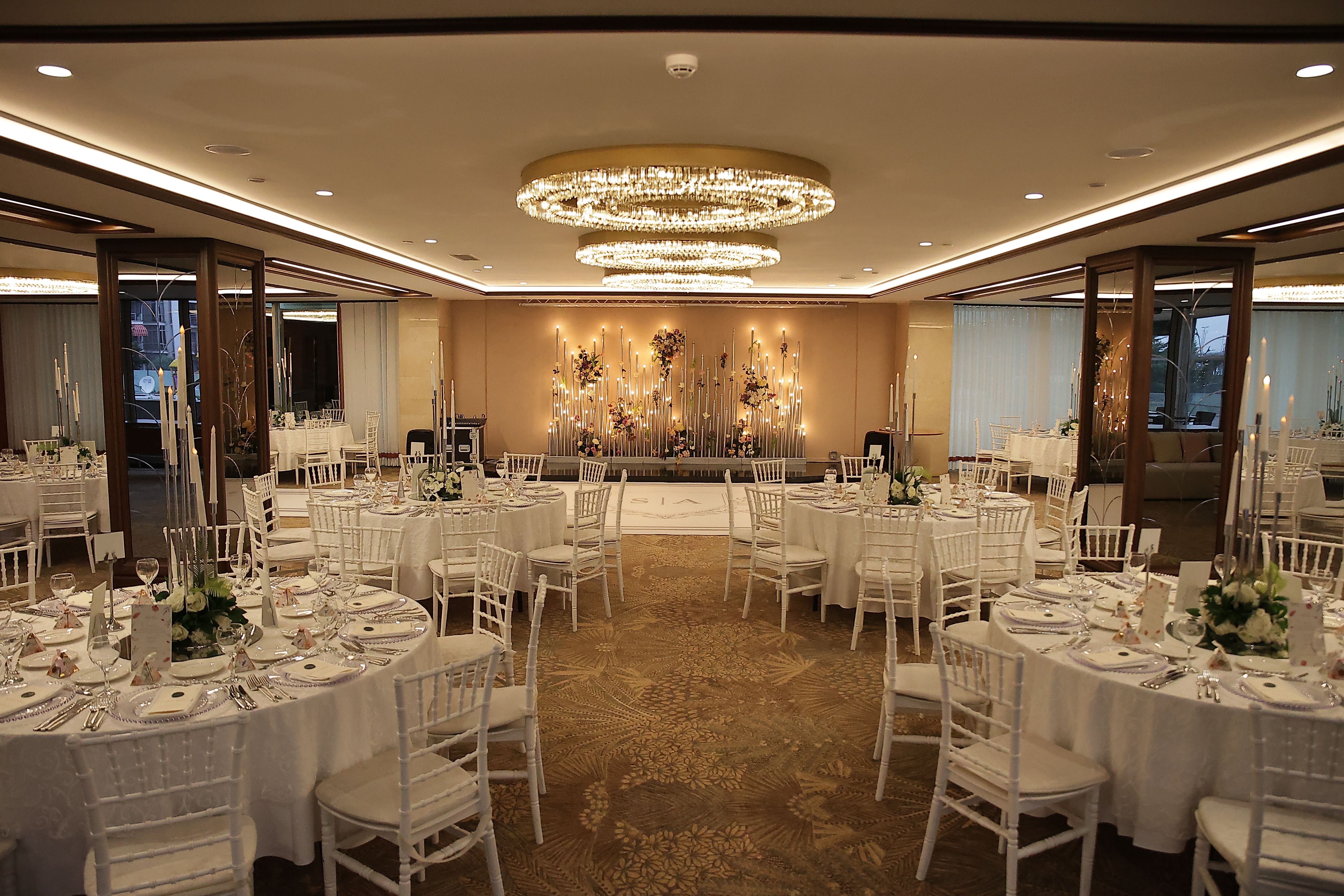 A grand ballroom decorated with round tables set for a formal event, featuring elegant chandeliers.