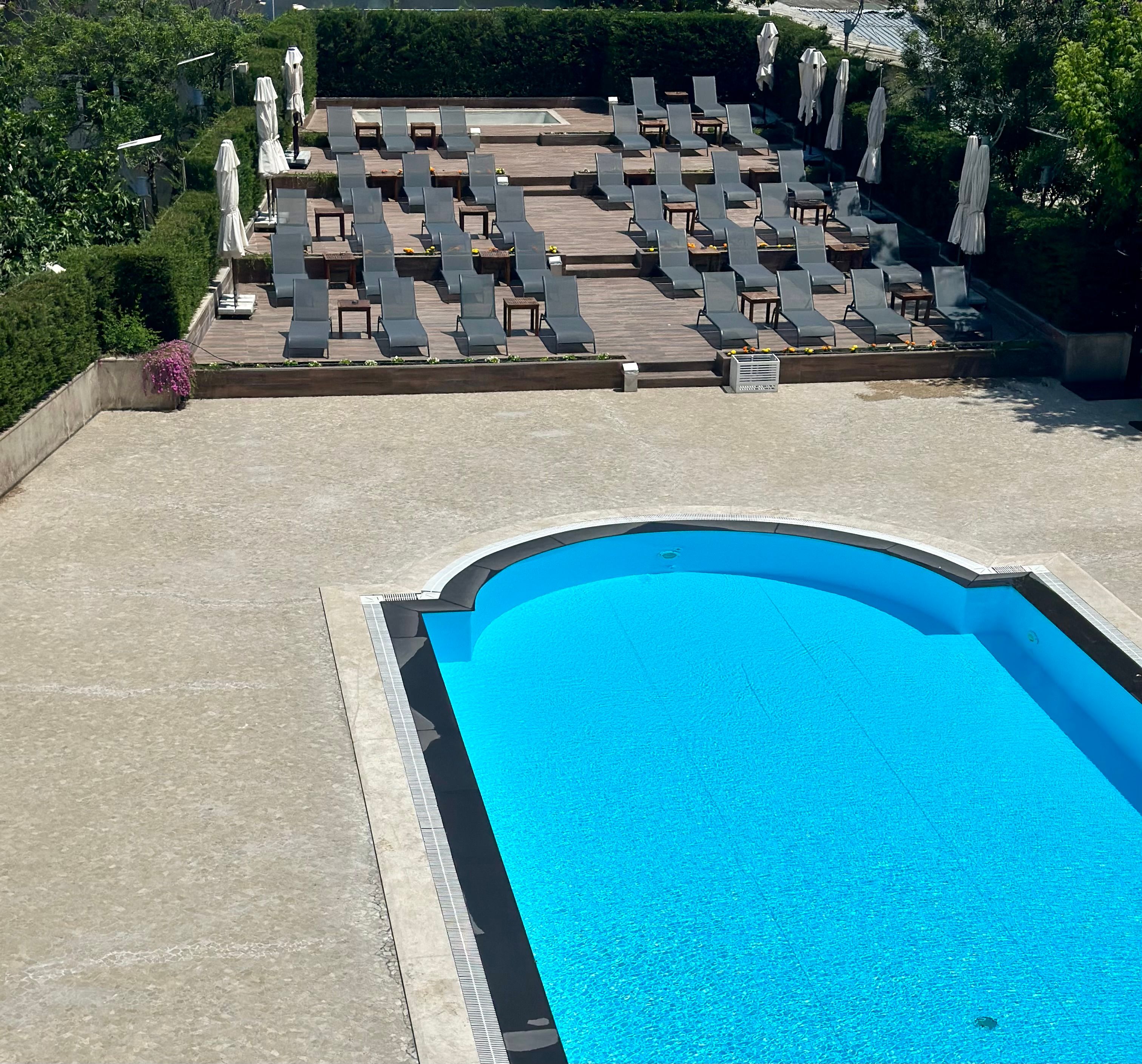 Empty swimming pool with many lounge chairs arranged on tiered levels.
