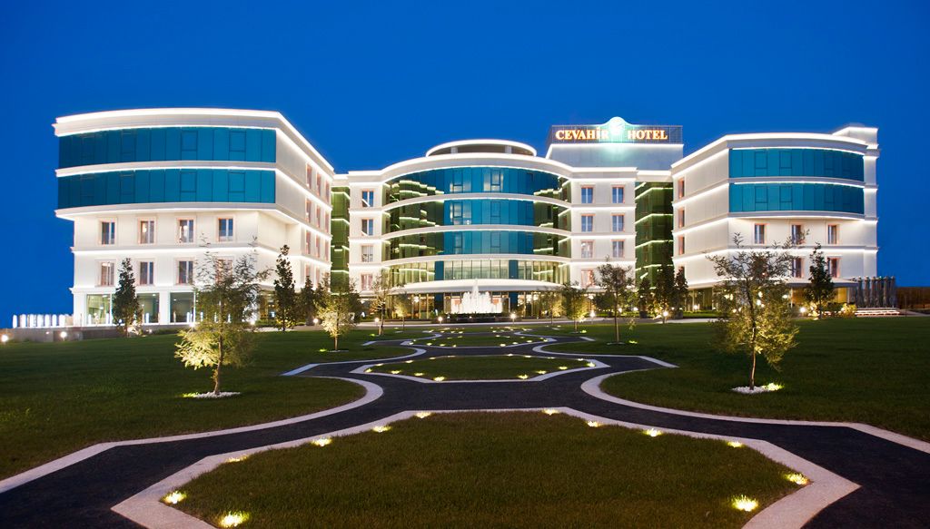 Modern hotel with glowing windows and manicured lawns at dusk.