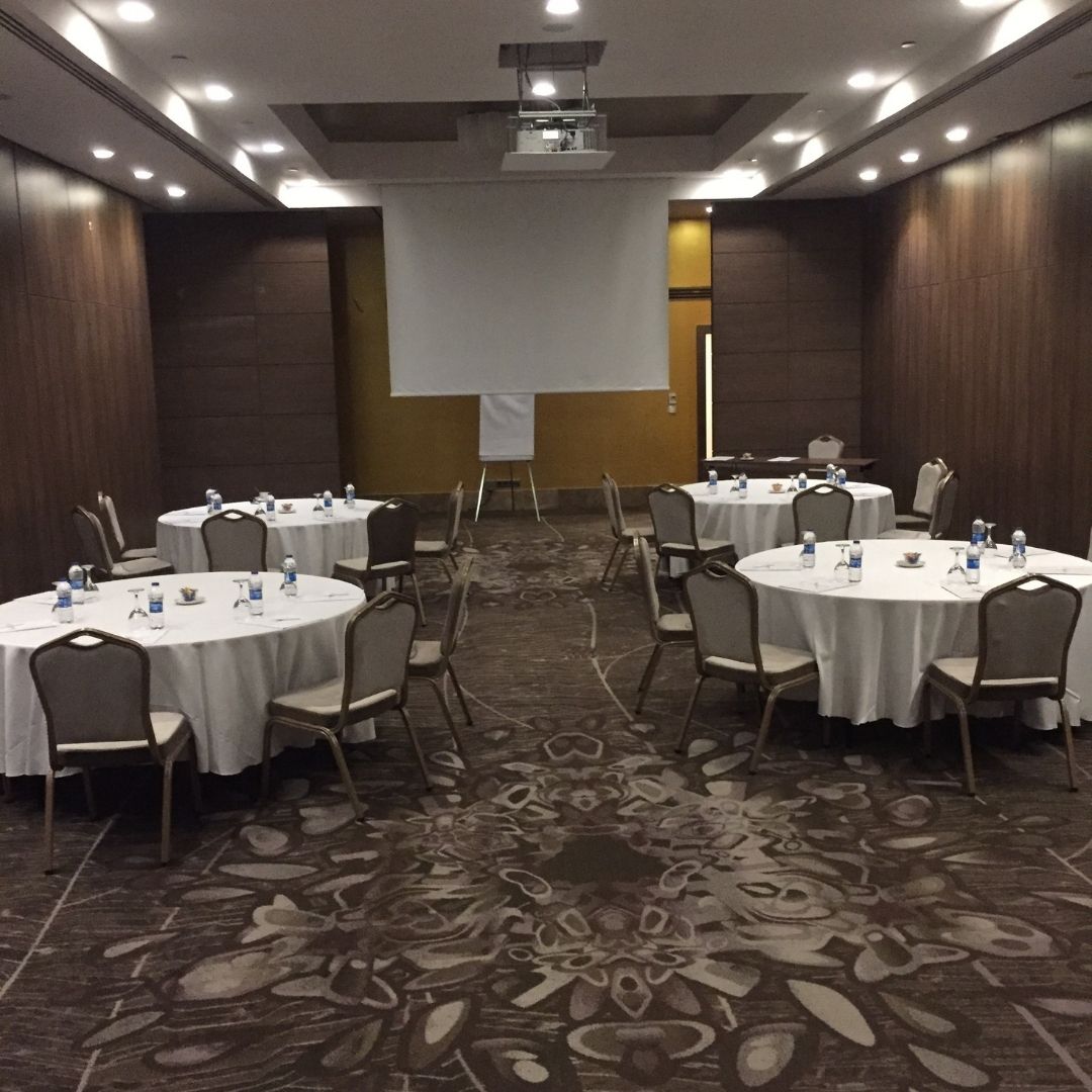 A conference room with round tables set for a meeting, equipped with a projector and screen.