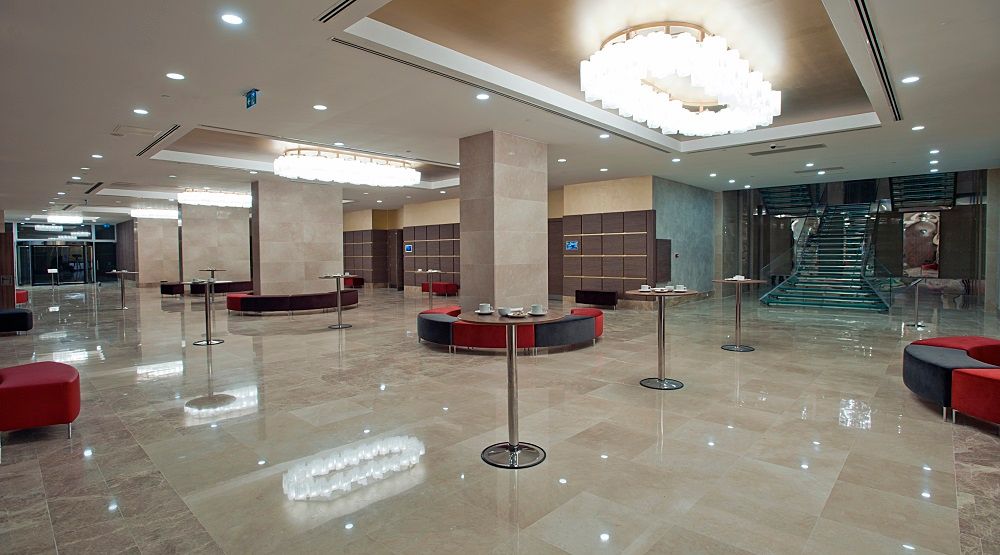 Modern hotel lobby with polished marble floors, elegant chandeliers, and red seating areas.