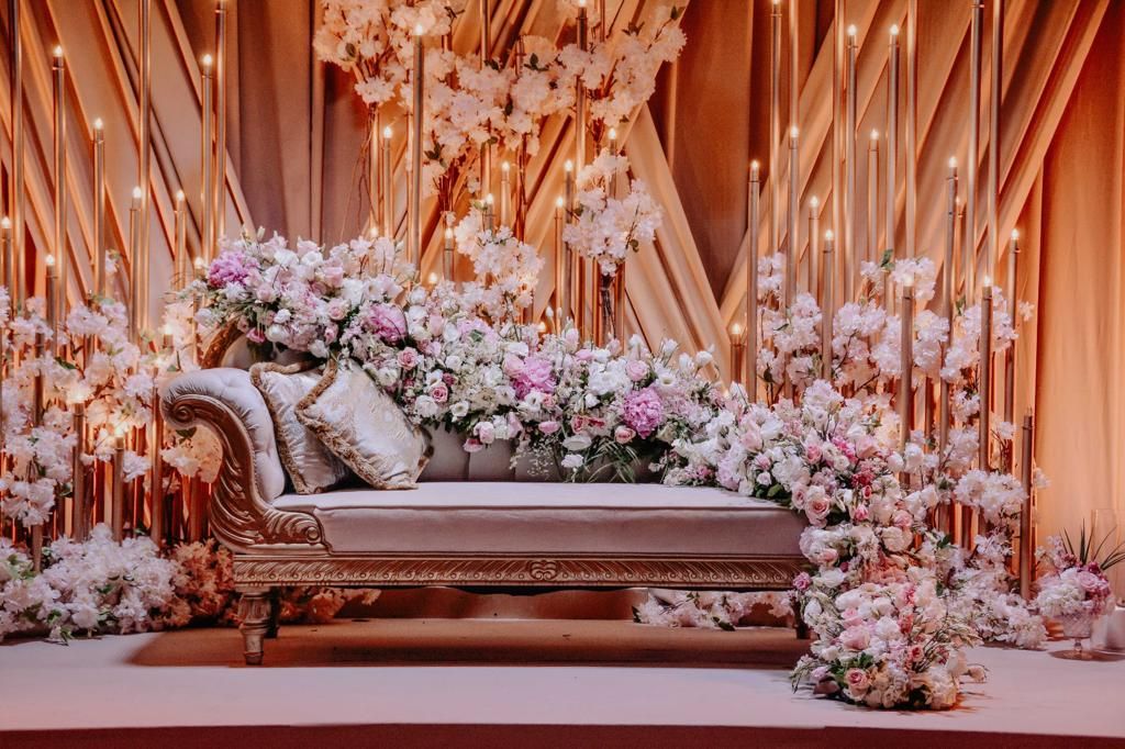 A luxurious chaise lounge is covered in abundant pink and white flowers for a wedding stage.