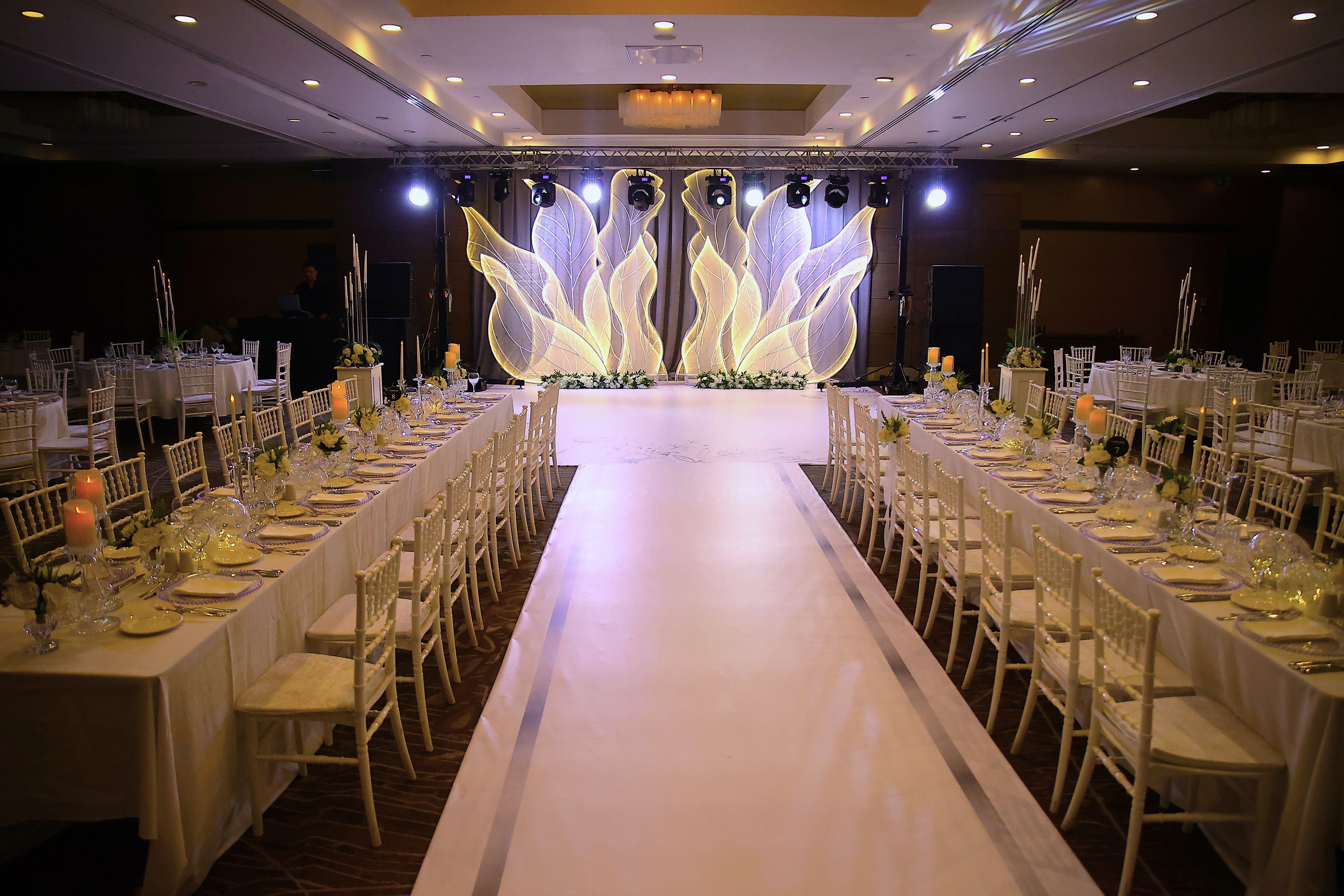 A banquet hall with long tables set for a formal event, leading to a decorated stage.
