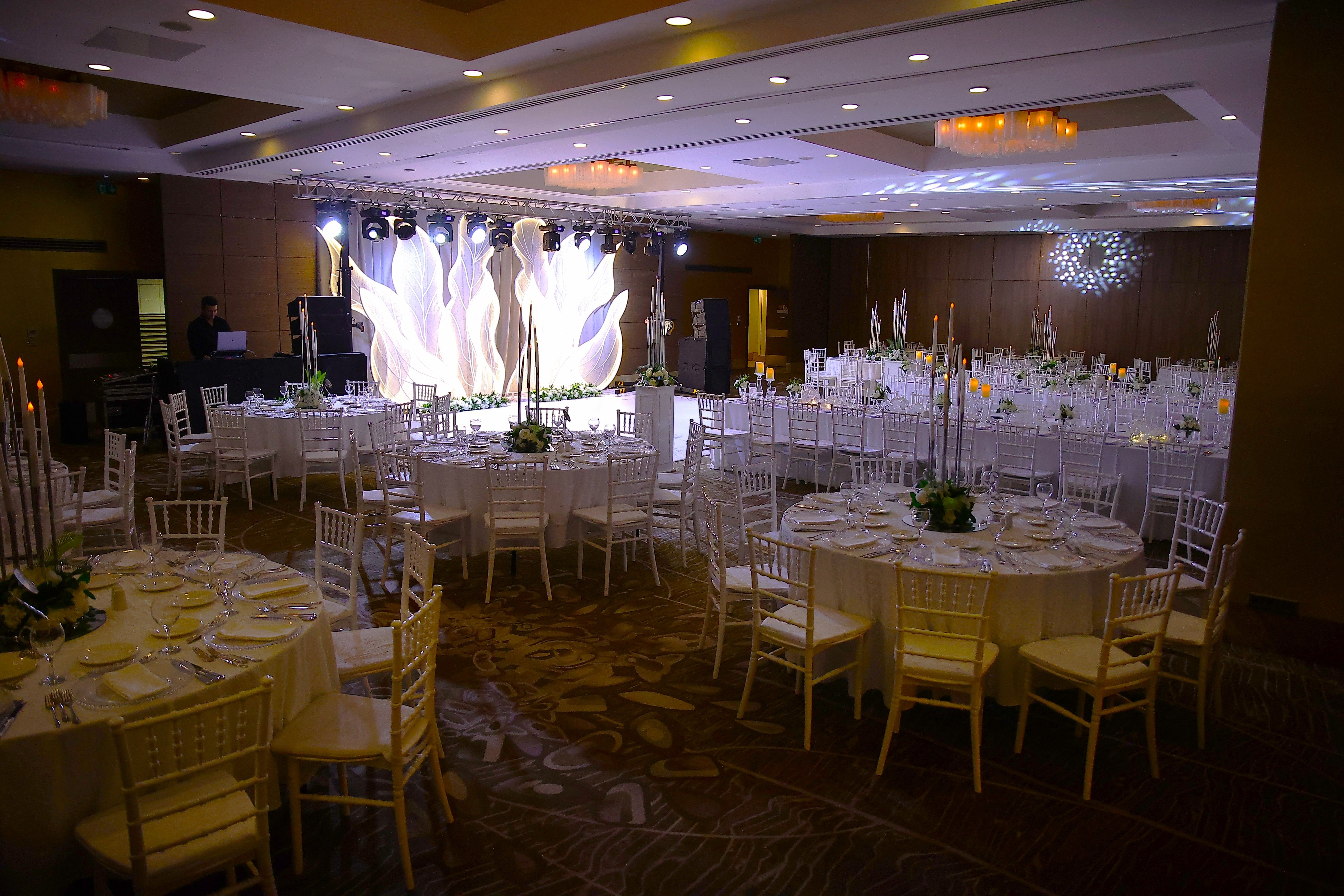 An elegant banquet hall prepared for an event with numerous white-clothed tables and chairs.