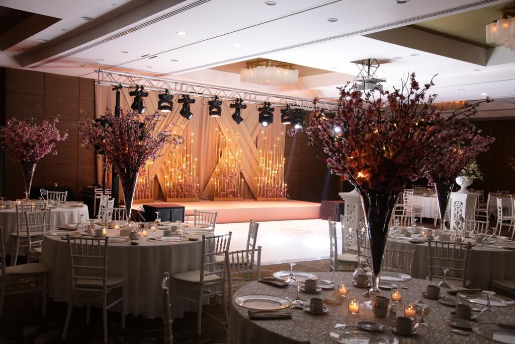 Elegantly decorated ballroom with round tables set for a formal event, featuring floral centerpieces and a stage backdrop.