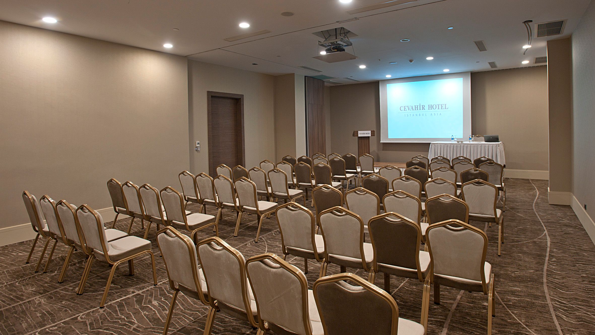 Empty conference room with rows of chairs facing a projector screen.