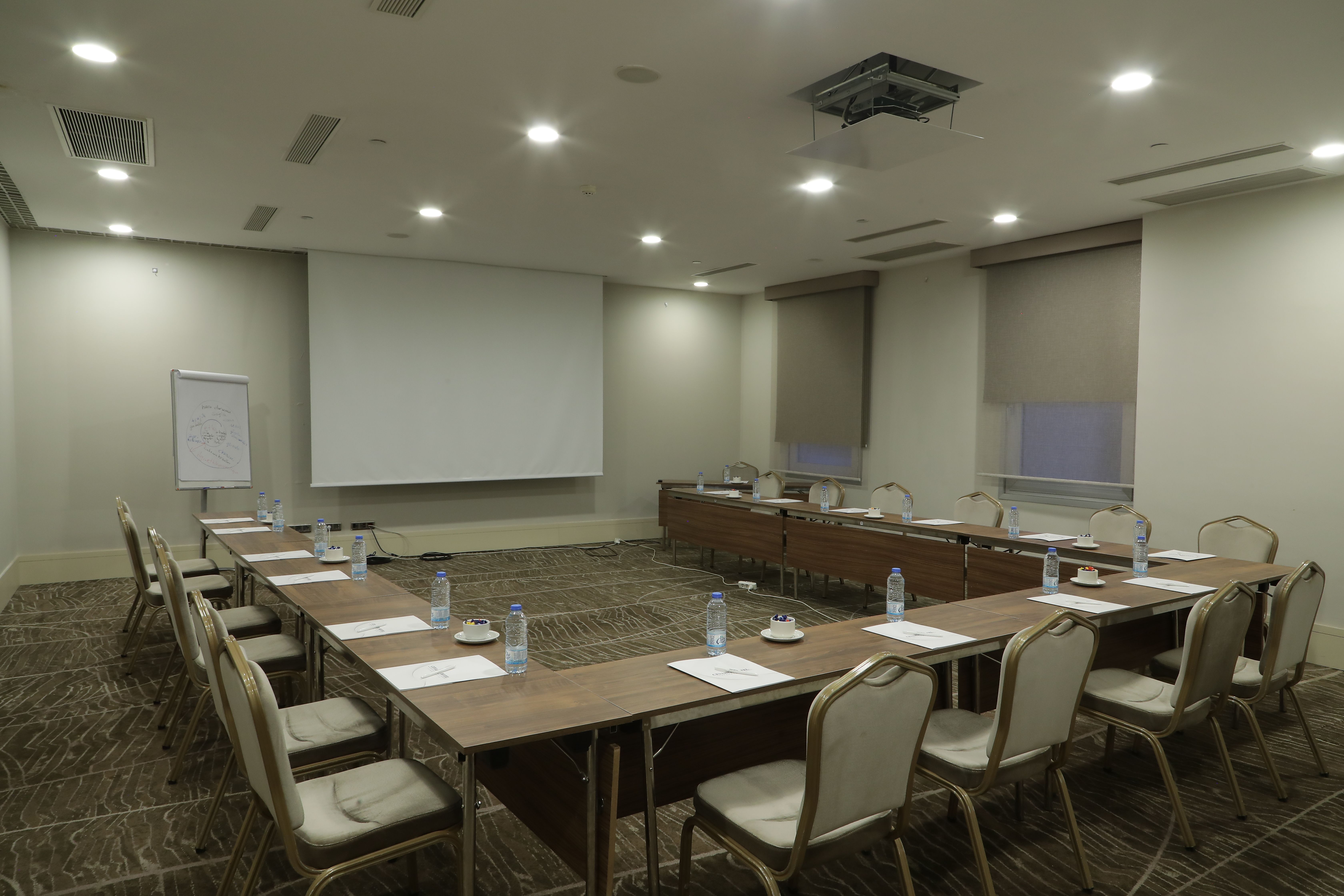 A U-shaped conference table is set for a meeting with chairs, water bottles, and notepads on the table.