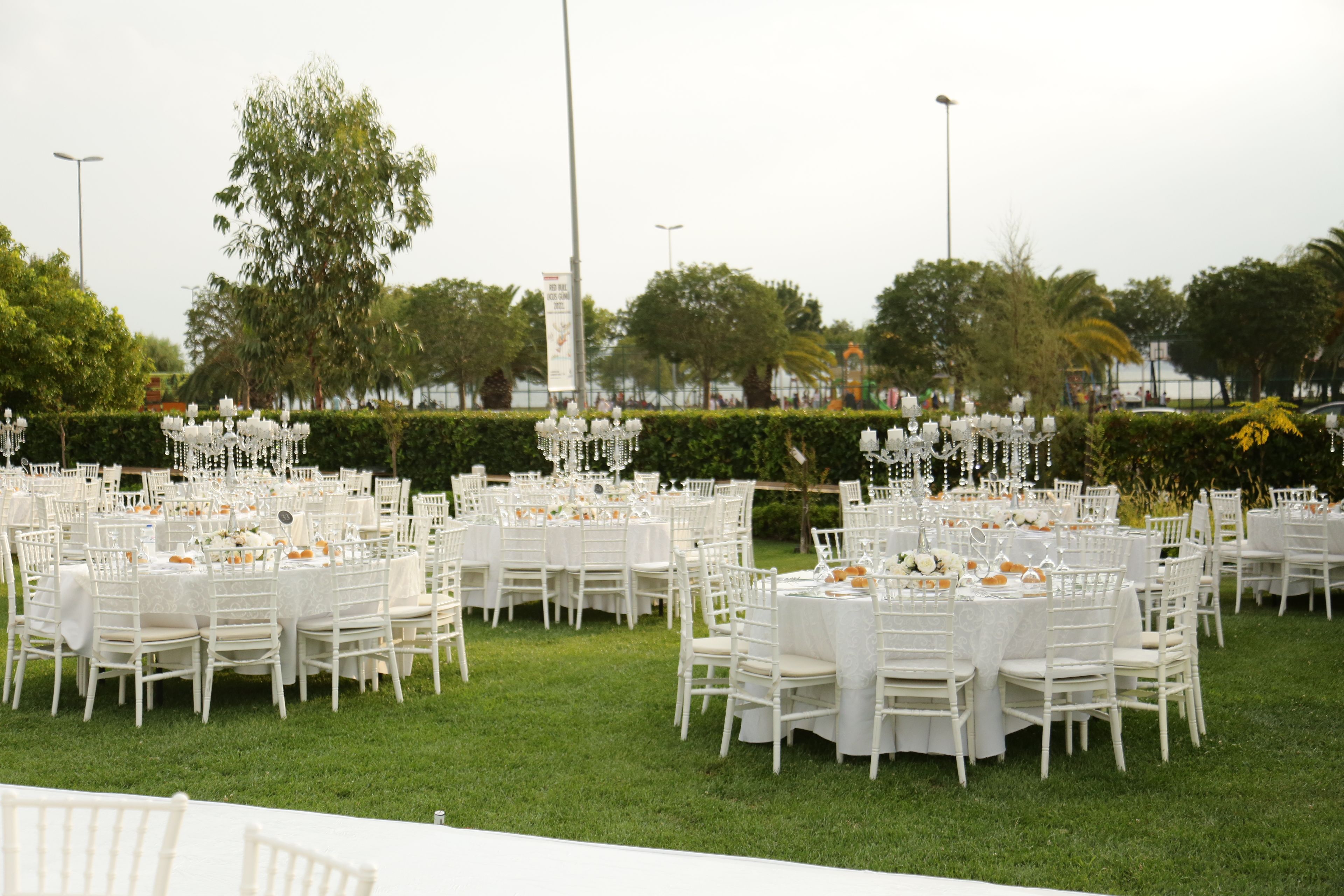 Outdoor event setup with numerous round tables and white chairs on a green lawn.