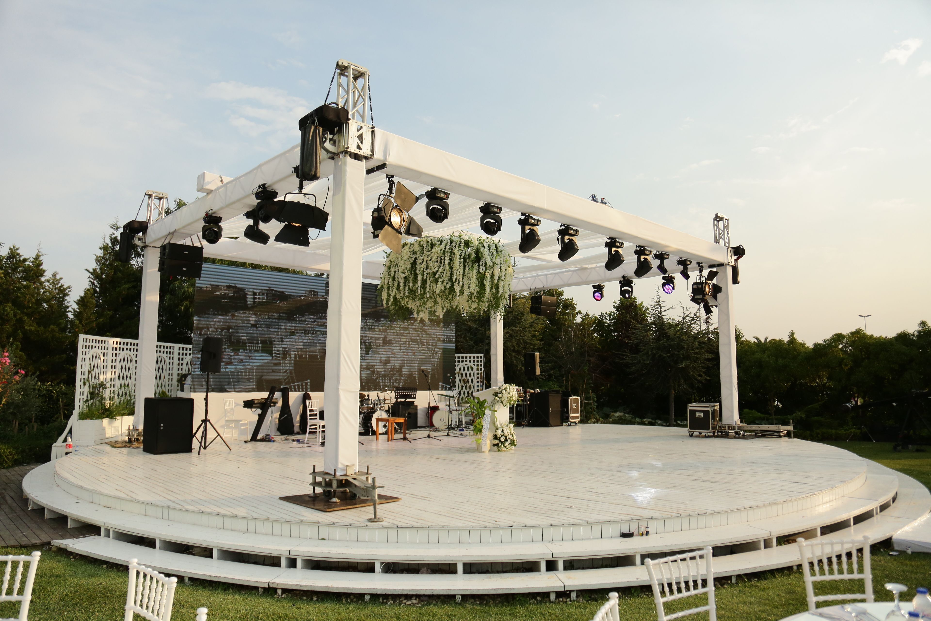 Outdoor stage with white flooring, lighting trusses, speakers, and a large screen.