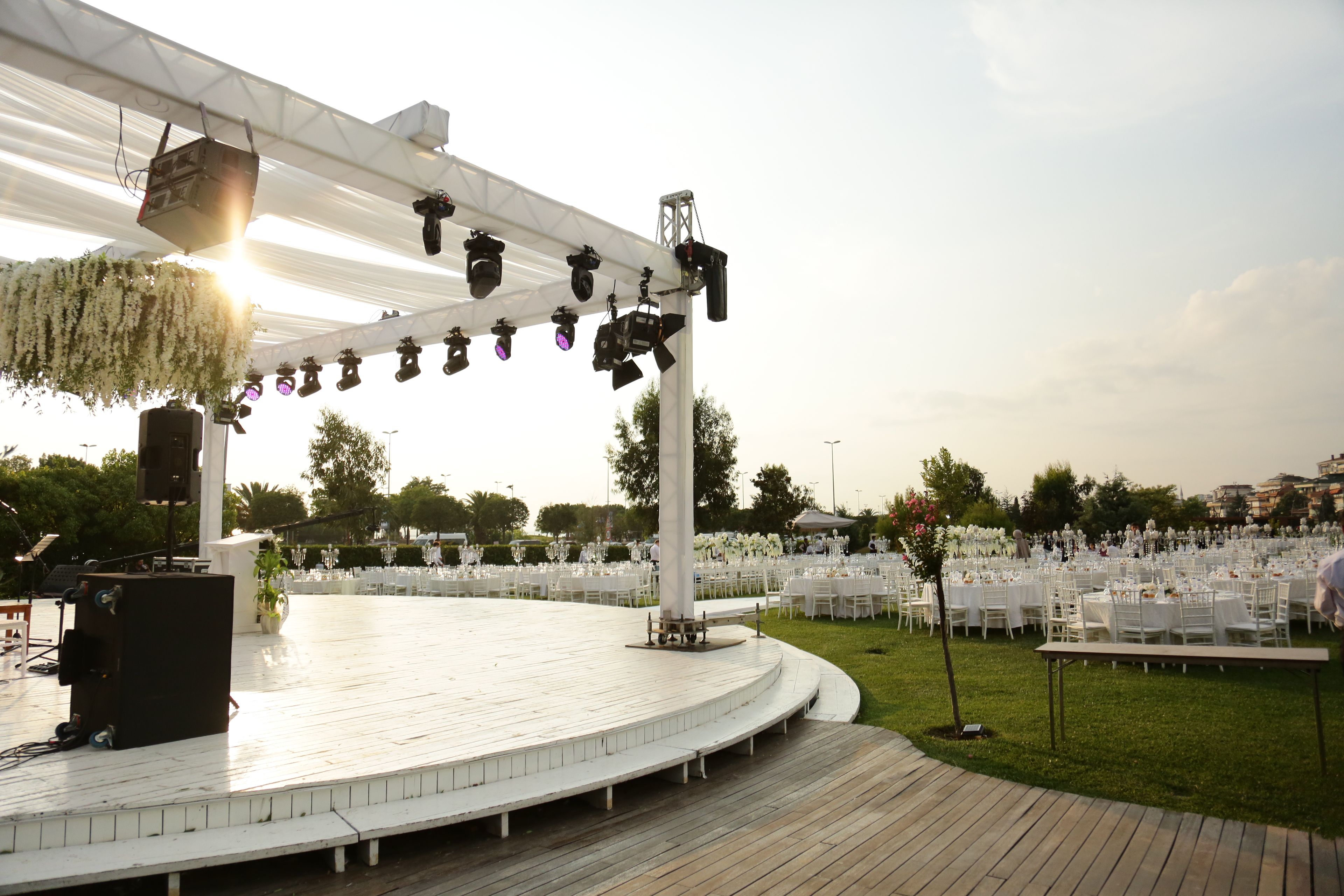 An outdoor wedding reception setup with a stage, white chairs, and tables on a grassy lawn.