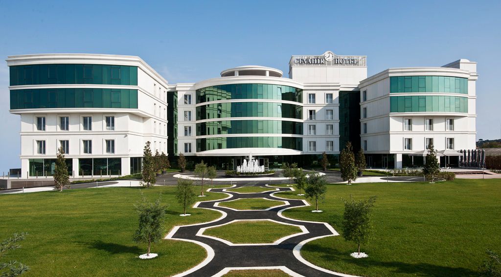 Modern hotel building with curved glass facades and white exterior walls, set against a blue sky with a manicured lawn.