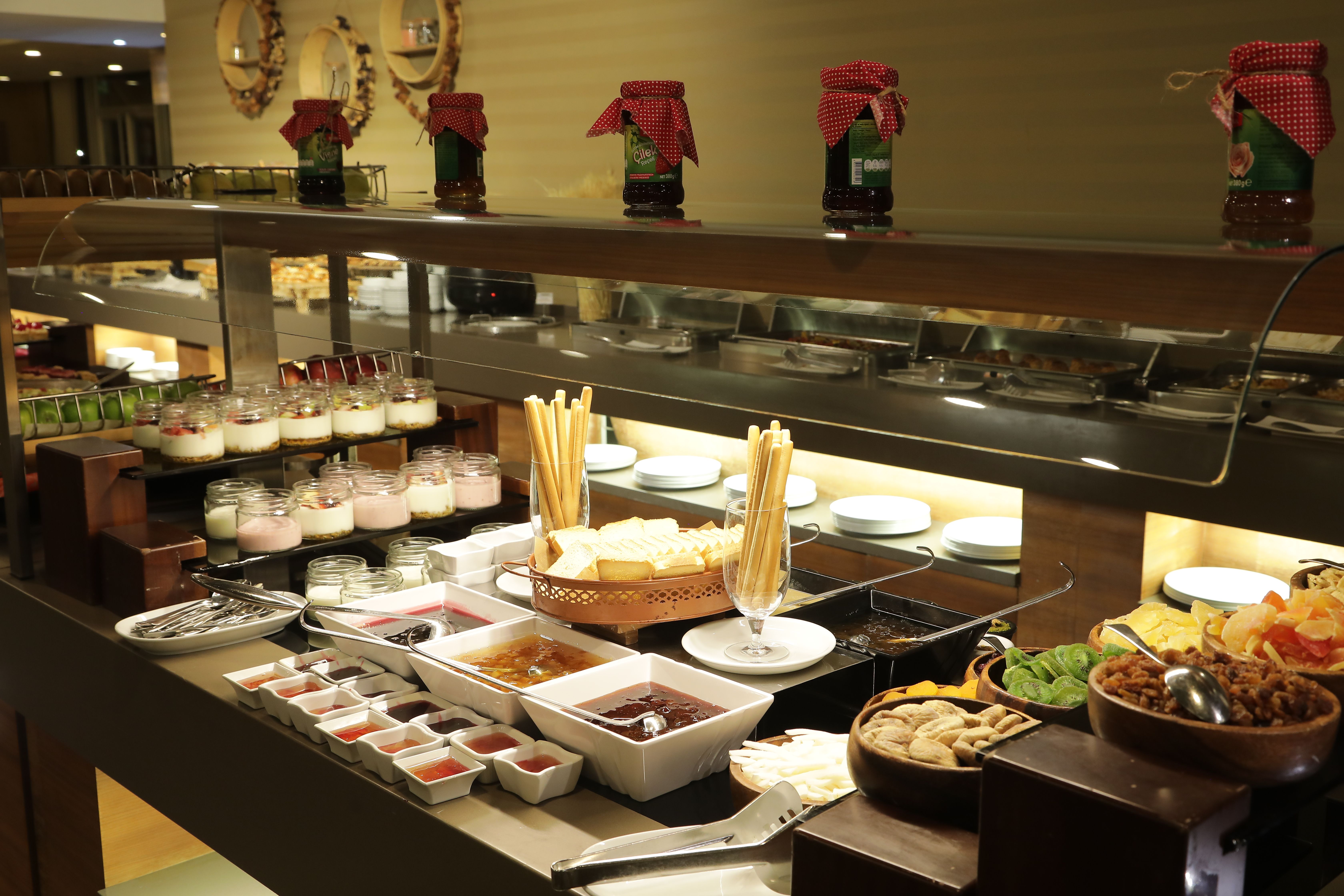 A buffet spread features various desserts, breadsticks, cheeses, and preserves.