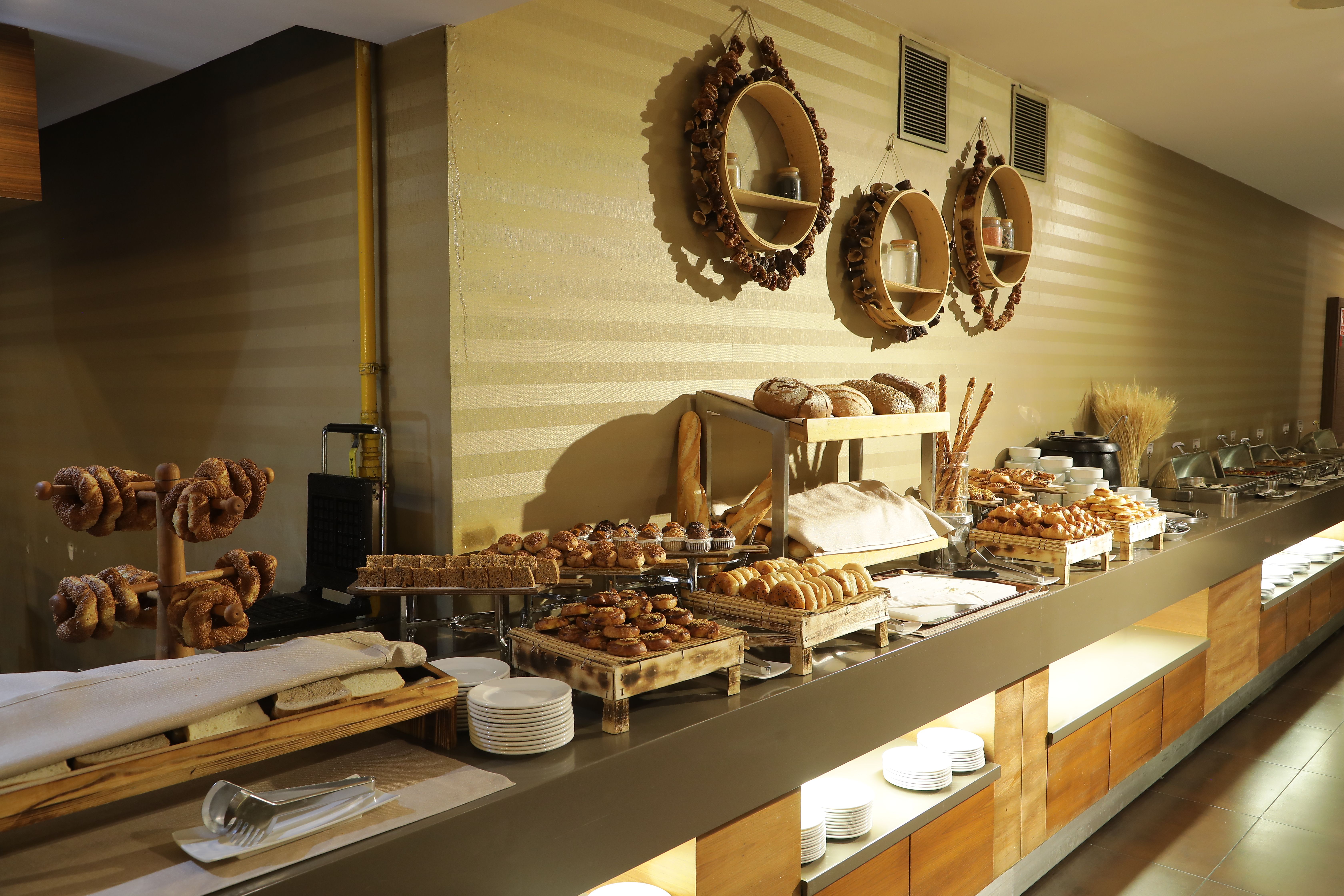 A long buffet table filled with assorted pastries, breads, and donuts for breakfast.