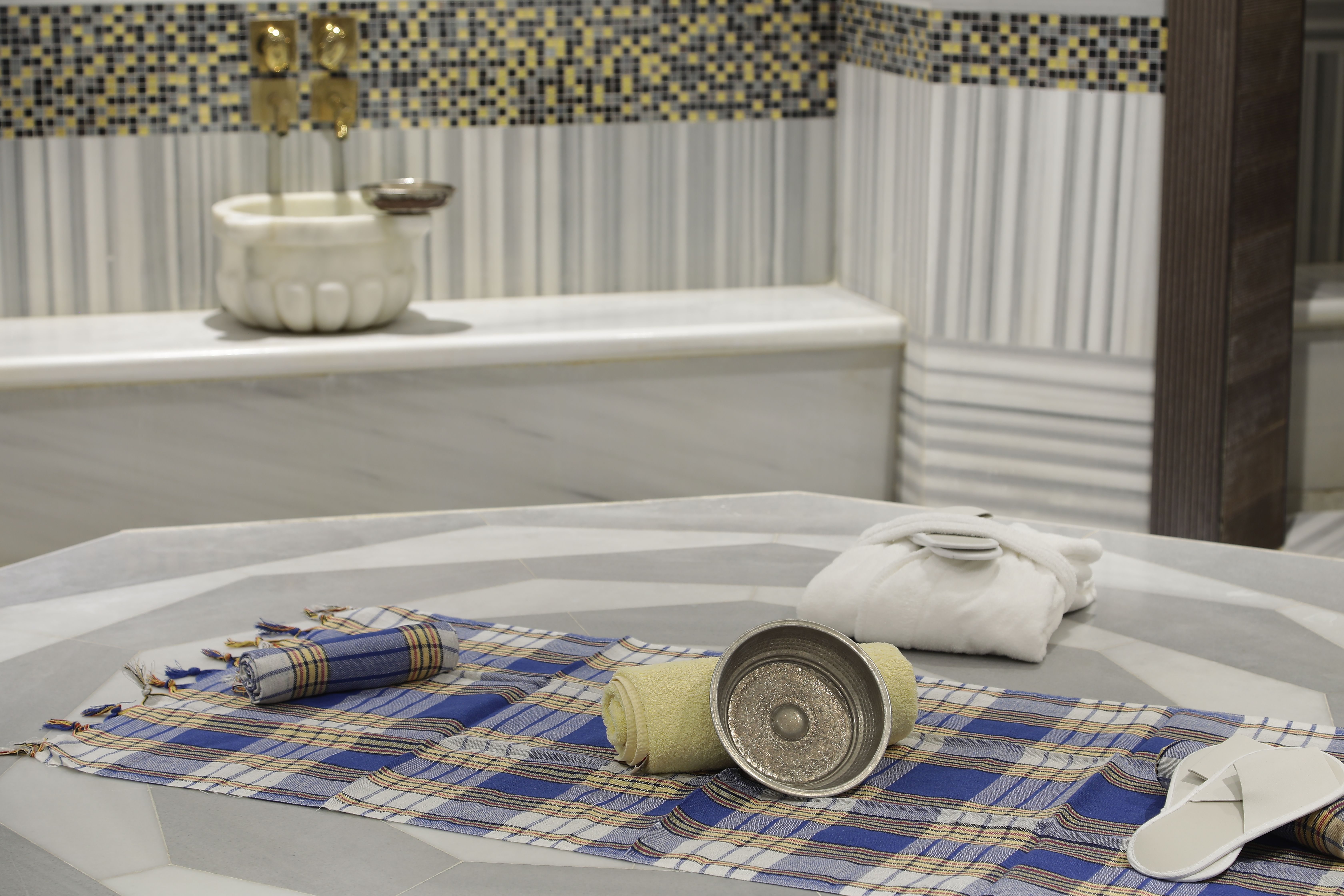 A traditional Turkish bath setting with marble surfaces, striped towels, and bathing accessories laid out.