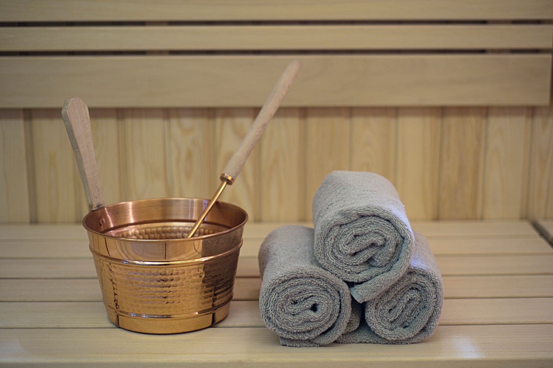 Copper bucket with ladle and rolled towels in a wooden sauna.
