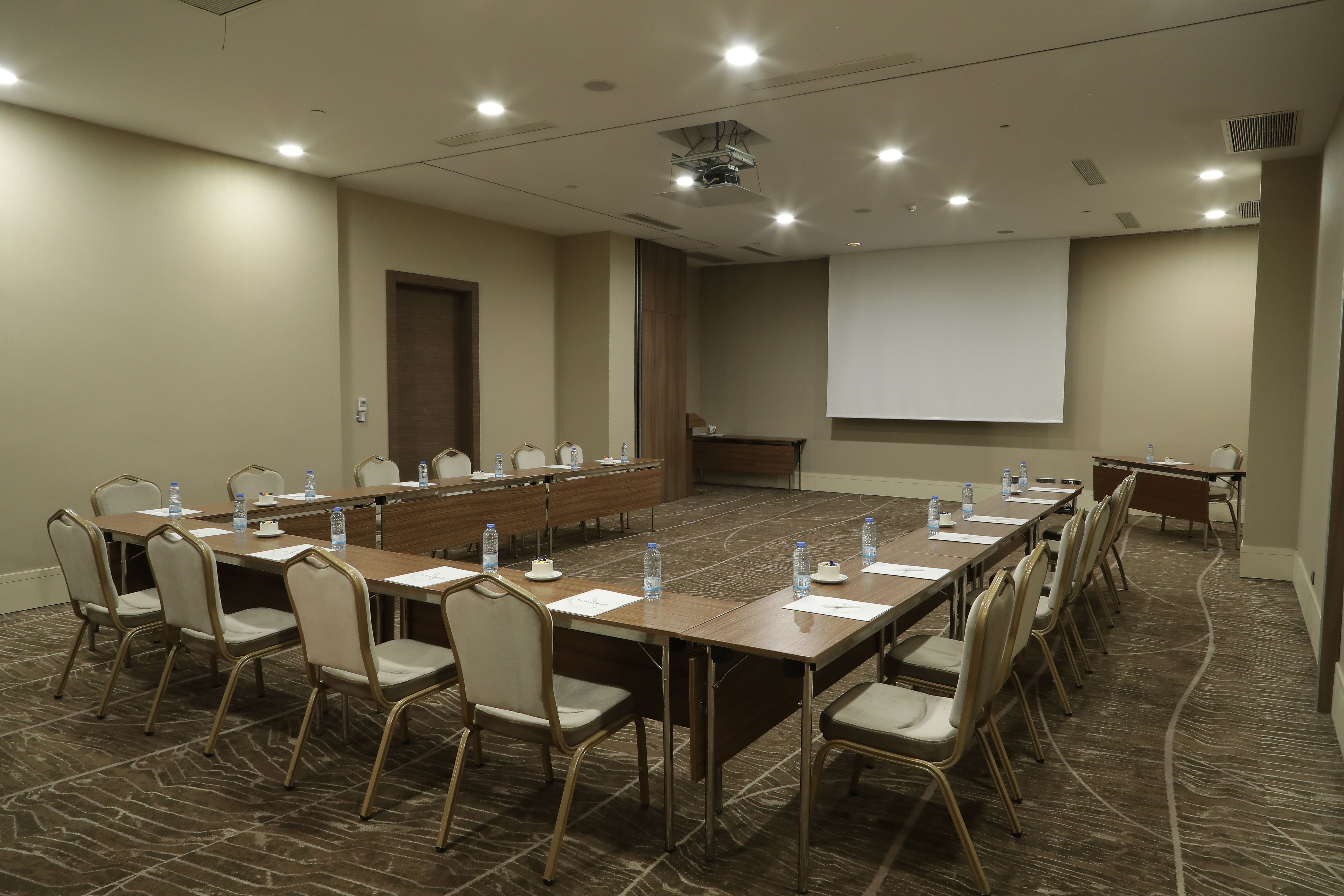 A modern meeting room with a U-shaped table arrangement, chairs, and a large projection screen.