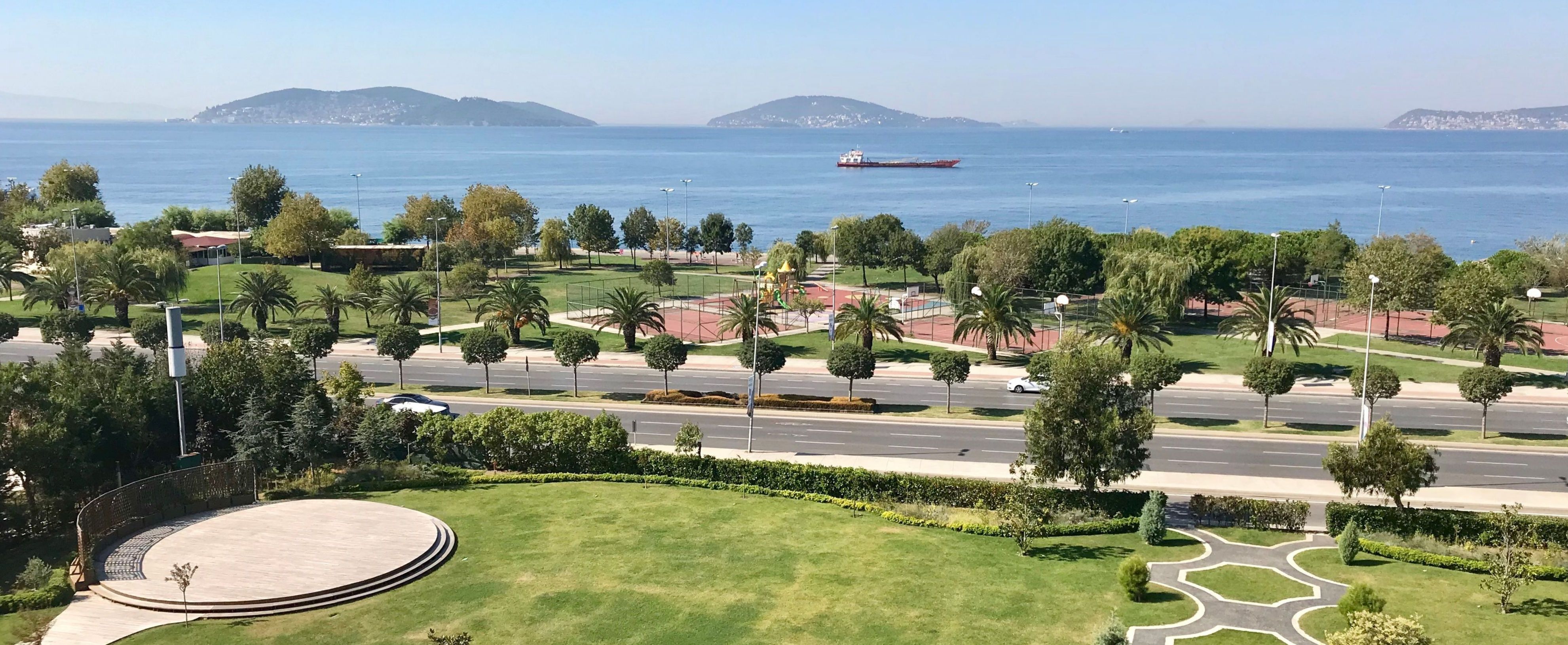 A scenic view of a green park with a clear blue sky and calm sea in the background.