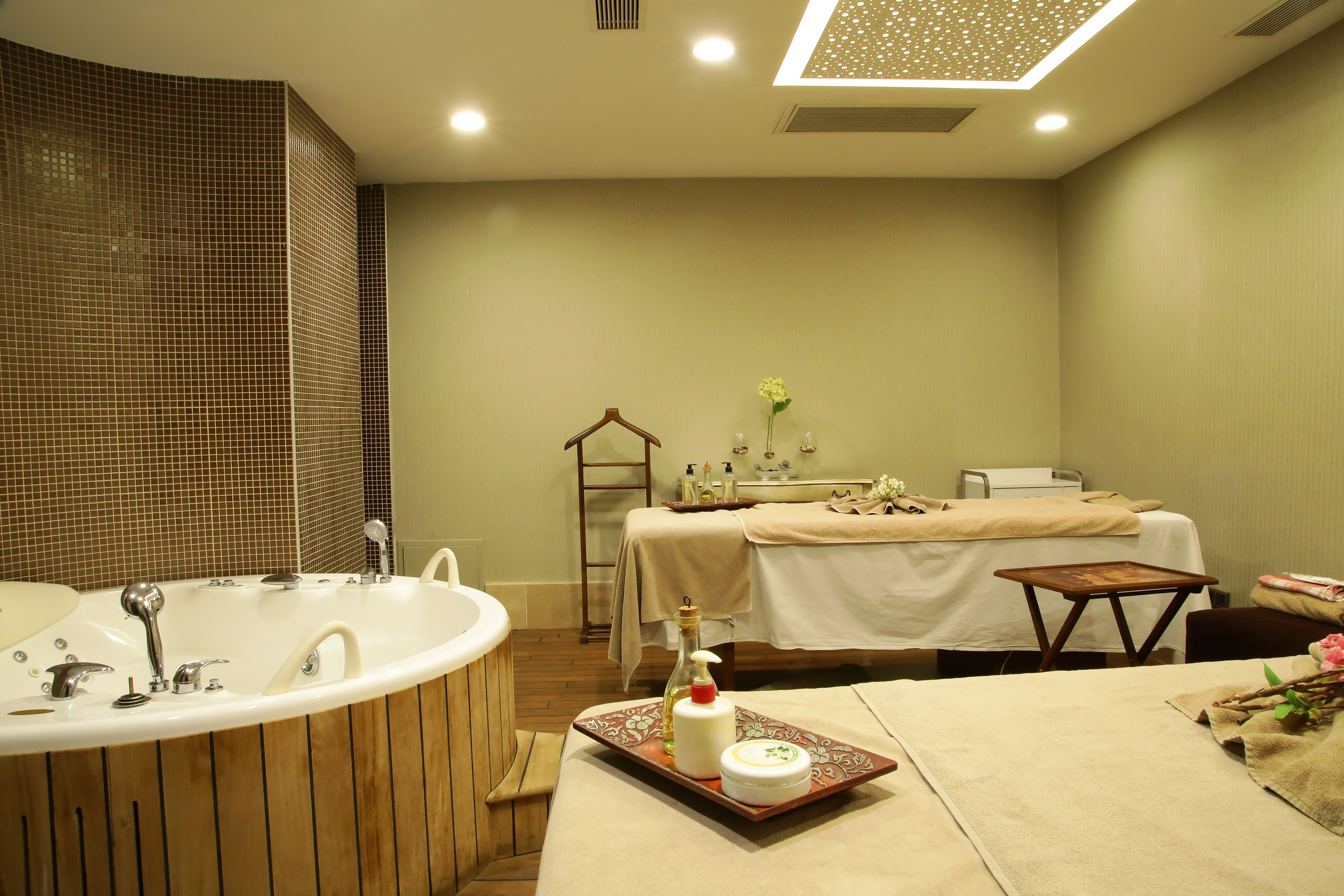 Spa room with two massage tables, a large bathtub, and ambient lighting.