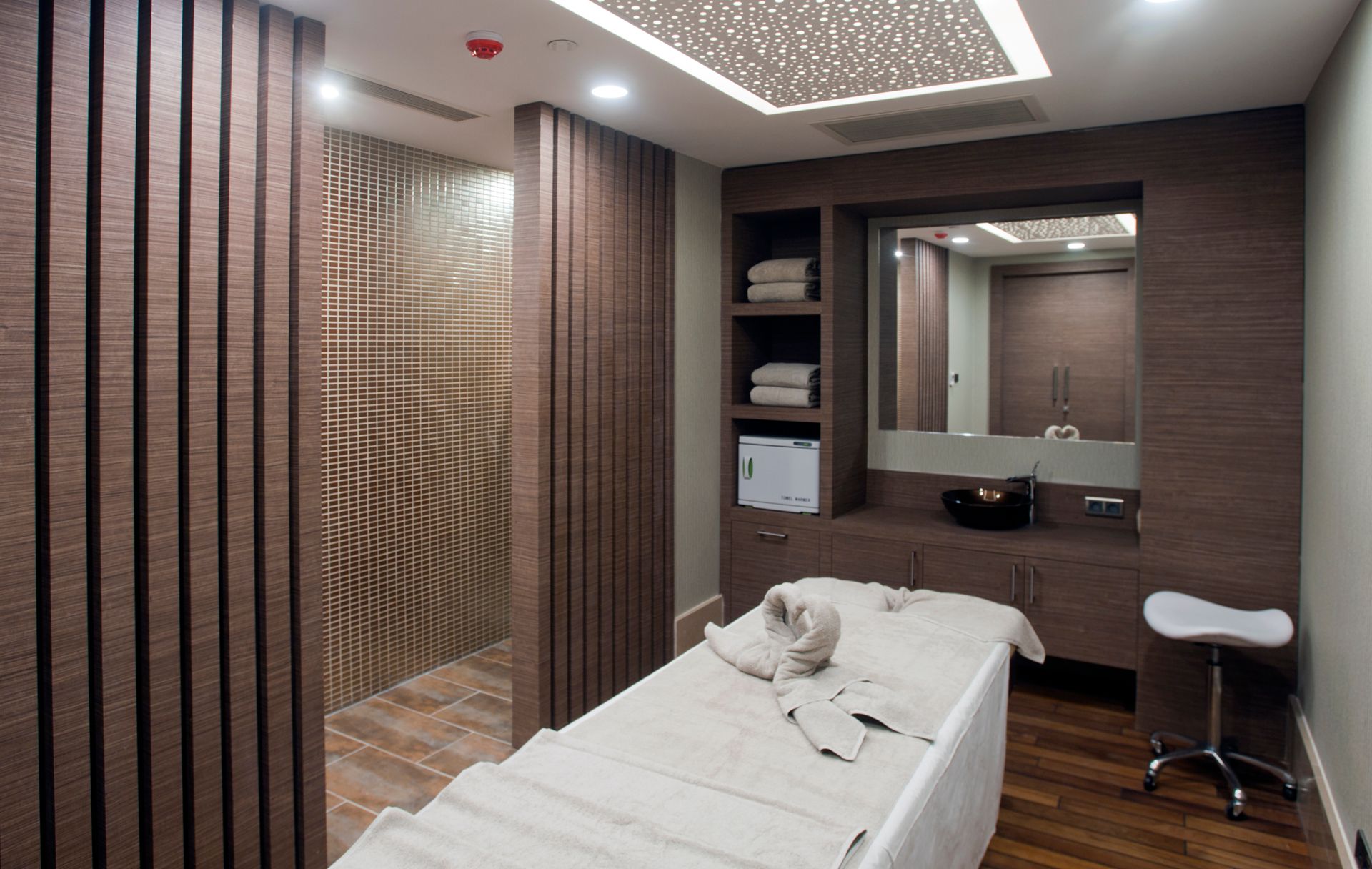 A massage table is set up in a spa room with wood paneling and a modern design.