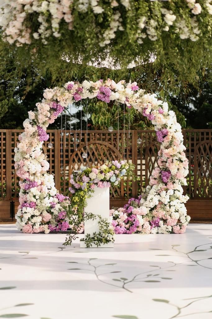 A circular floral archway adorned with white and purple flowers, framing a small white cake.