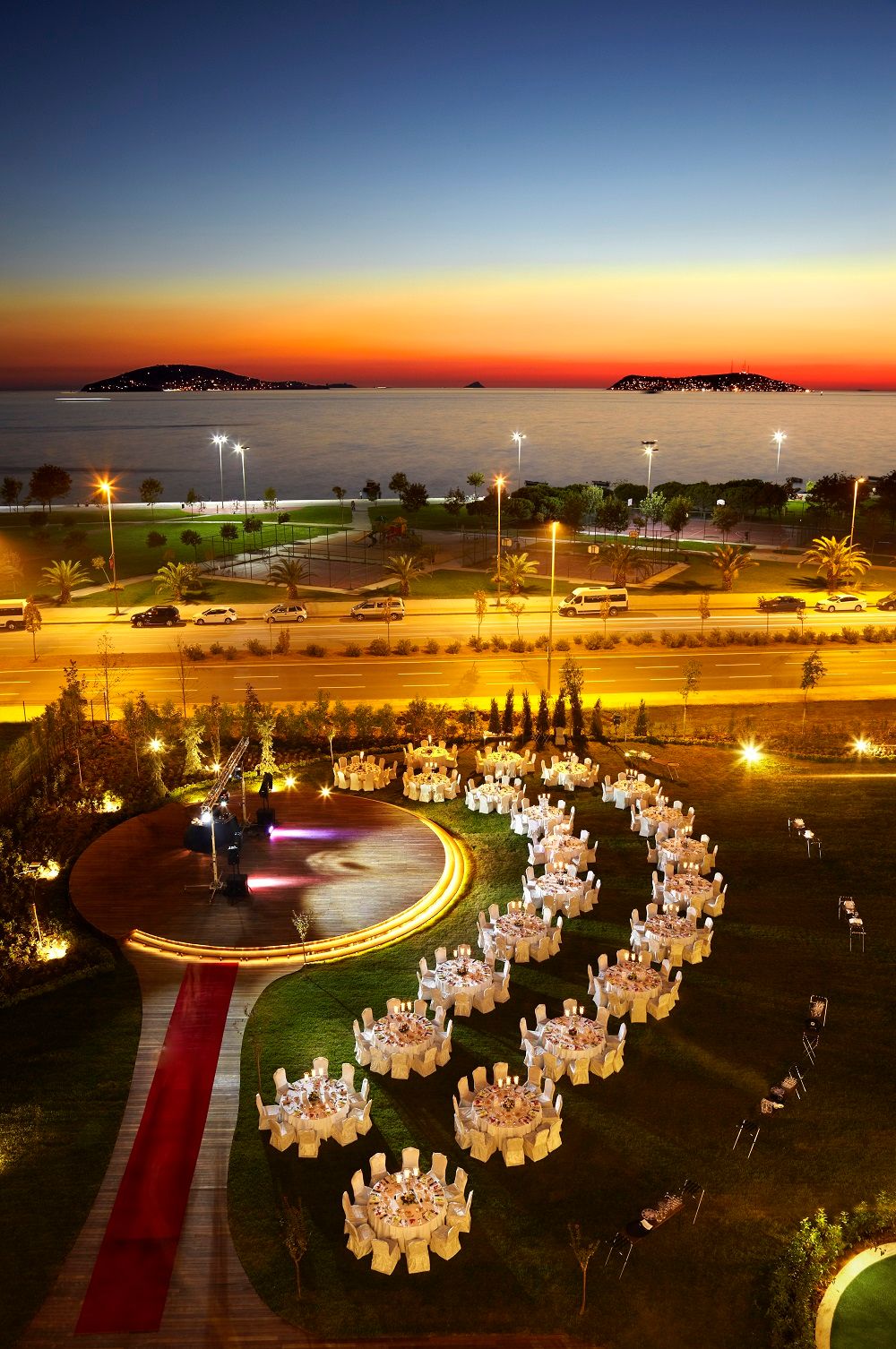 Outdoor dining tables set up on a lawn by the water at sunset.