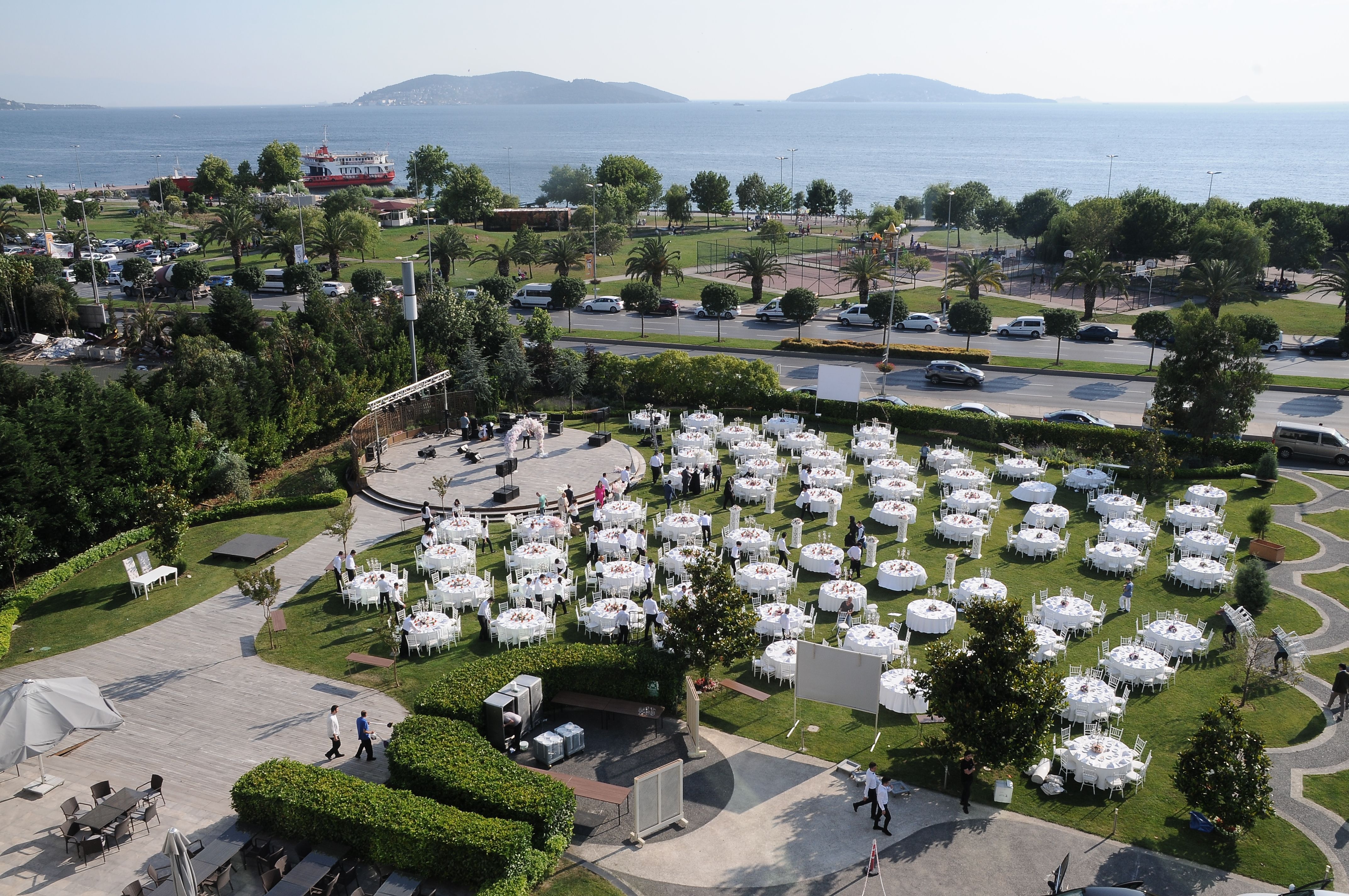 Outdoor event with many white tables in a garden overlooking the sea.
