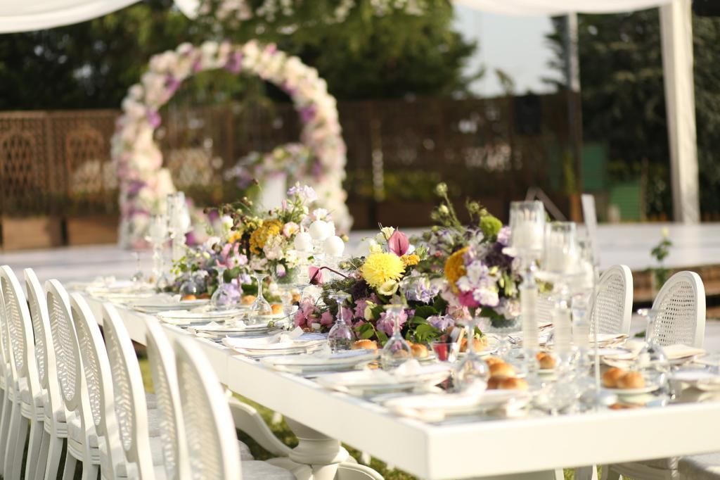 Elegant outdoor dining table with colorful floral centerpieces, white chairs, and a floral arch.