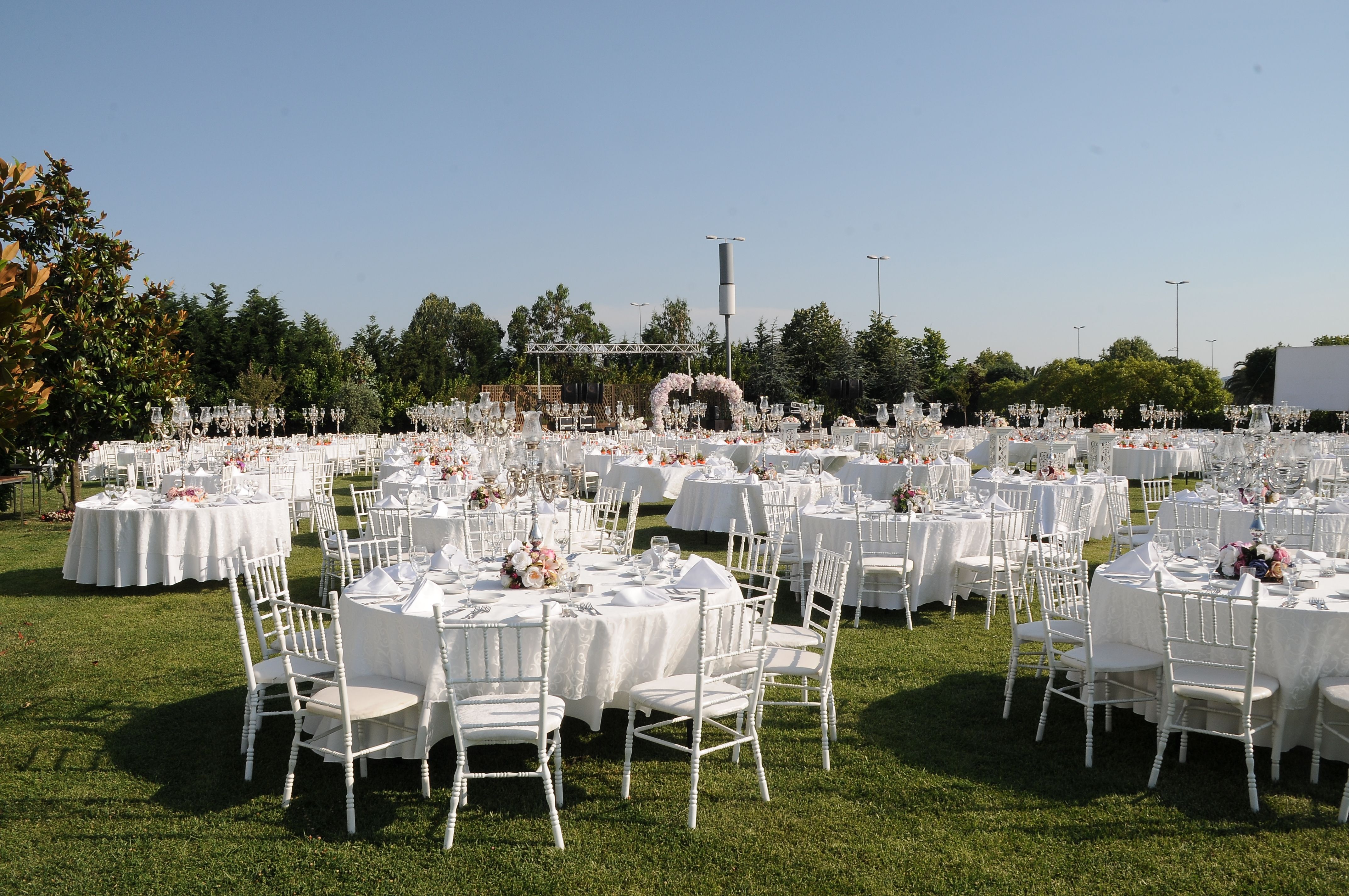 Outdoor wedding reception with white tables, chairs, and floral arch on a green lawn.