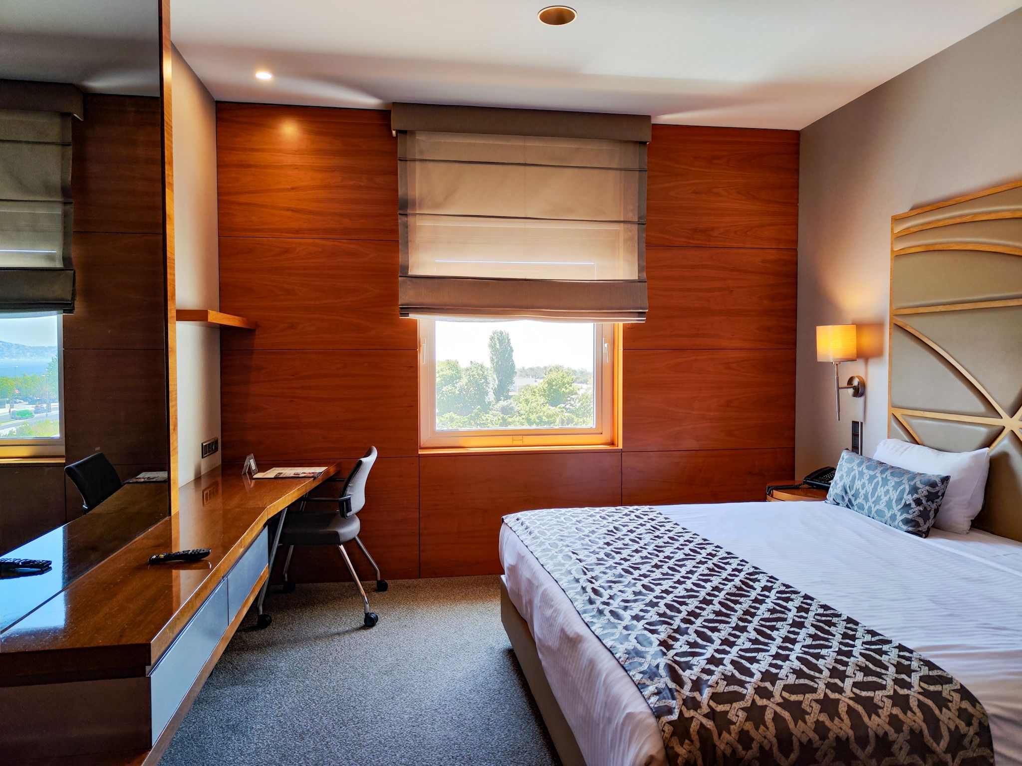 Modern hotel room with a neatly made bed, wooden walls, a desk, and window.