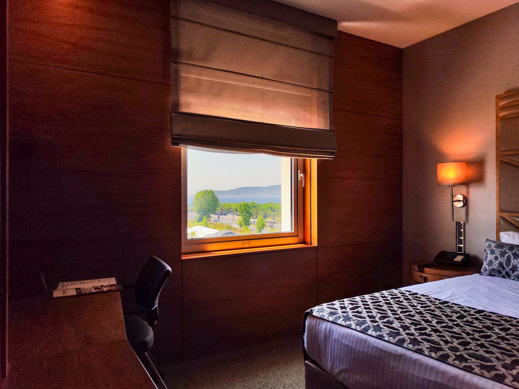 Modern hotel room featuring dark wood, a bed, desk, and window with a scenic view.