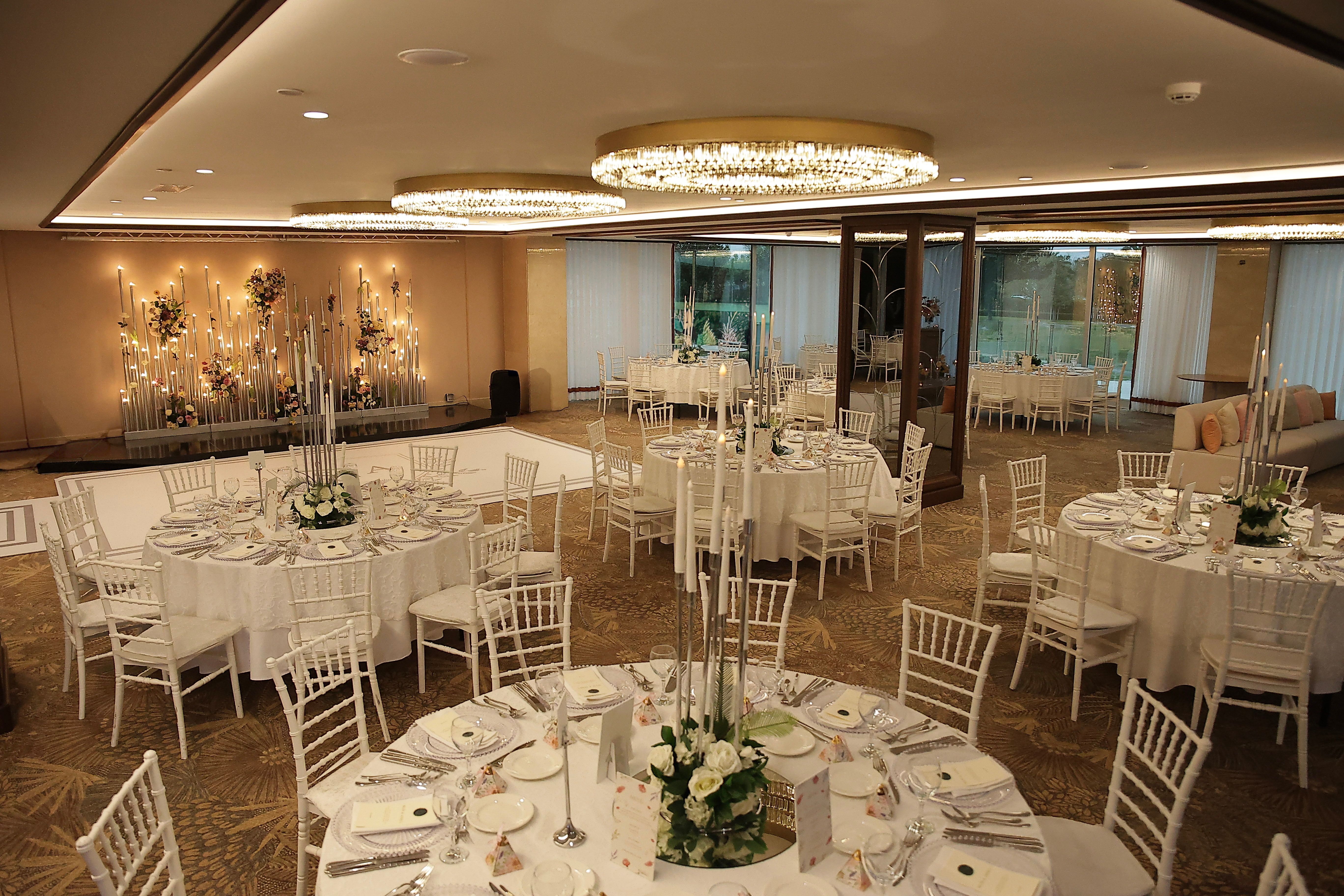 Elegant banquet hall with multiple round tables set for an event, featuring white decor.