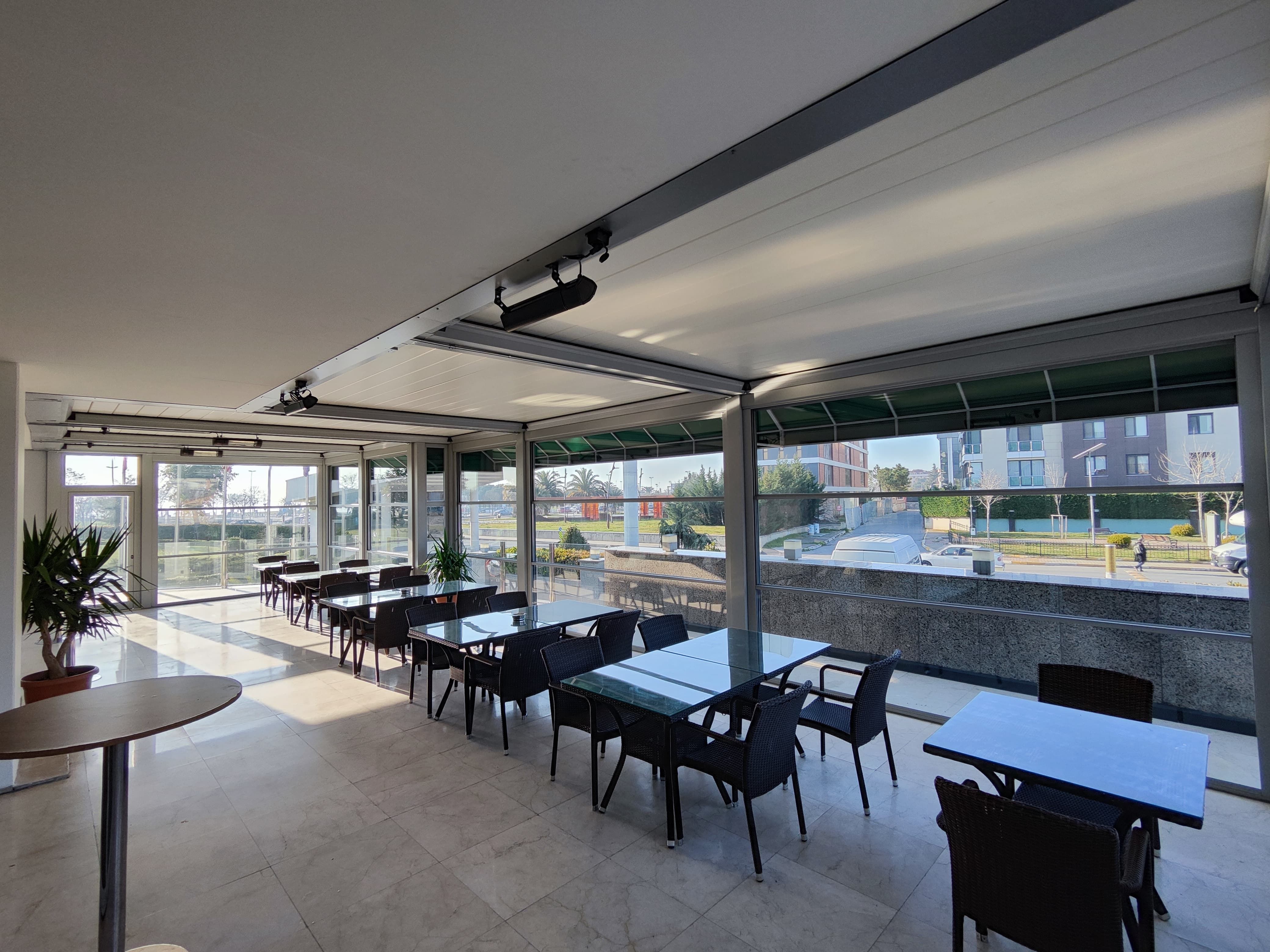 An expansive modern outdoor patio with dining tables, chairs, and a retractable roof system.