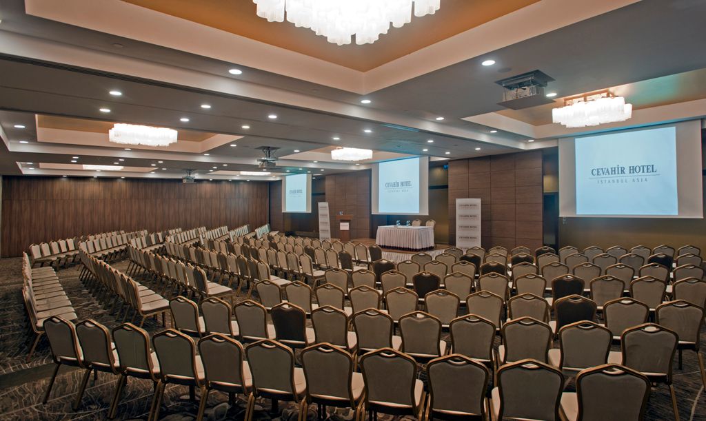 Spacious, empty conference room with curved rows of chairs facing presentation screens.