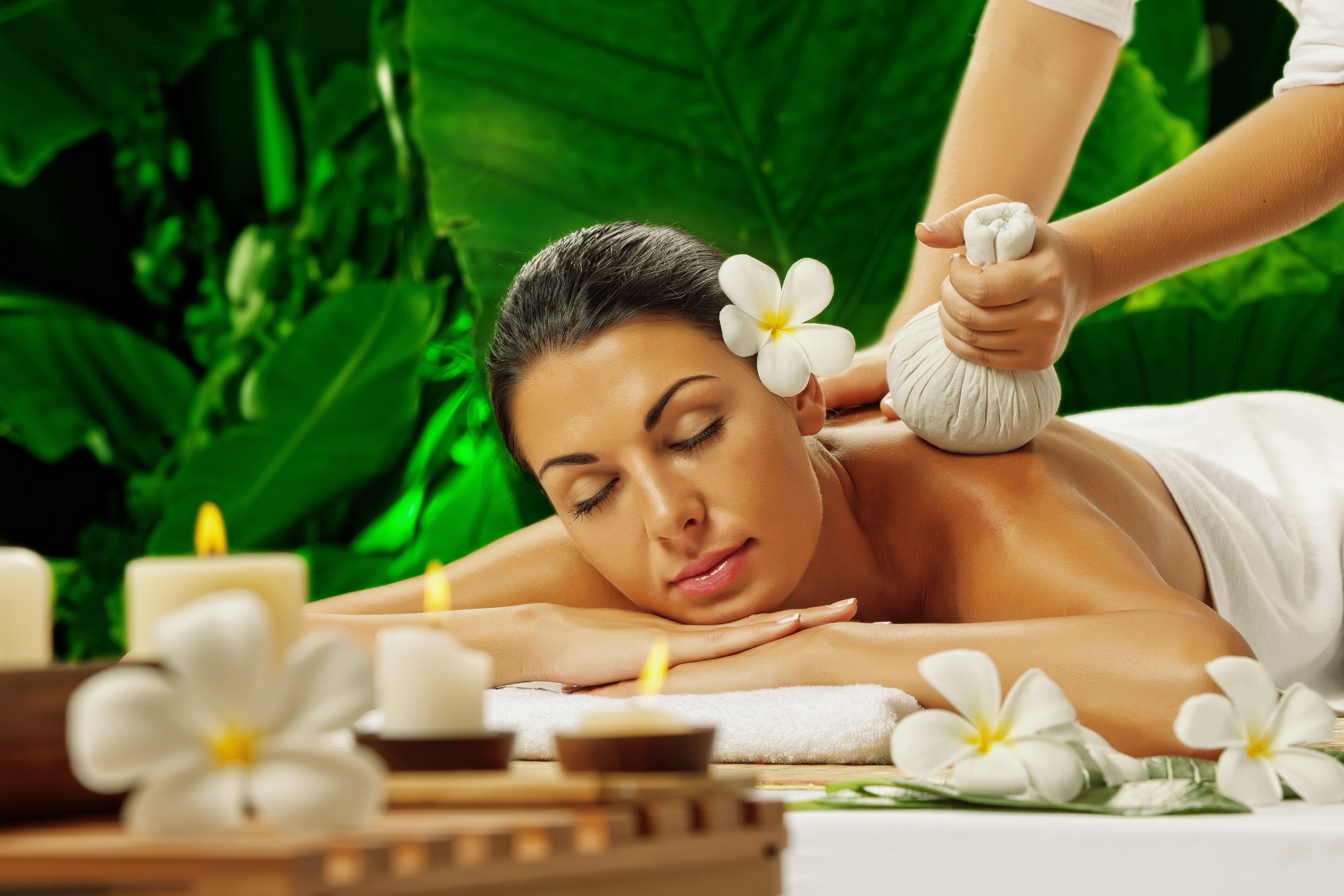 Woman receiving a herbal compress massage with candles and flowers nearby.