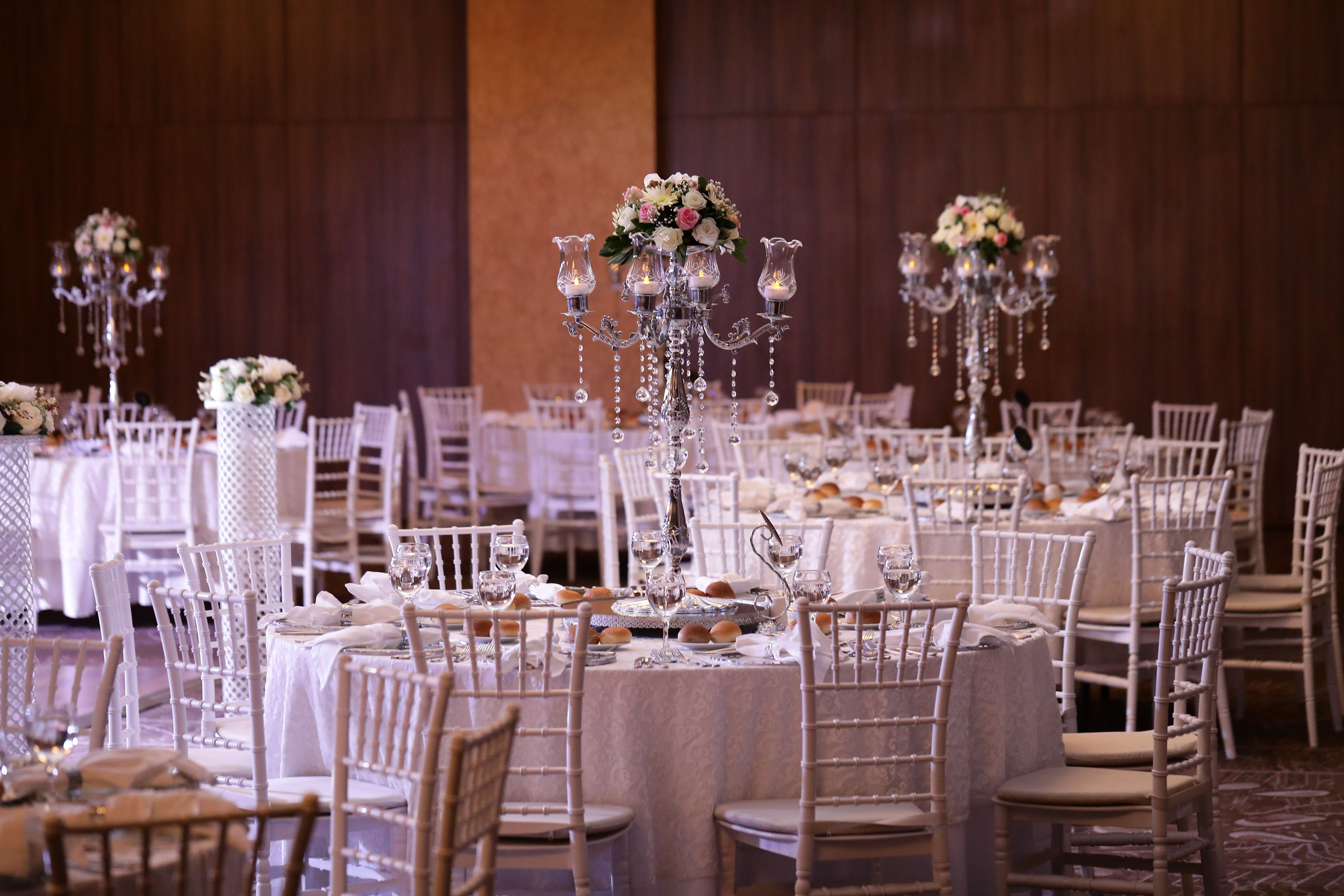 Formal event space with round tables, white chairs, and elaborate floral centerpieces.
